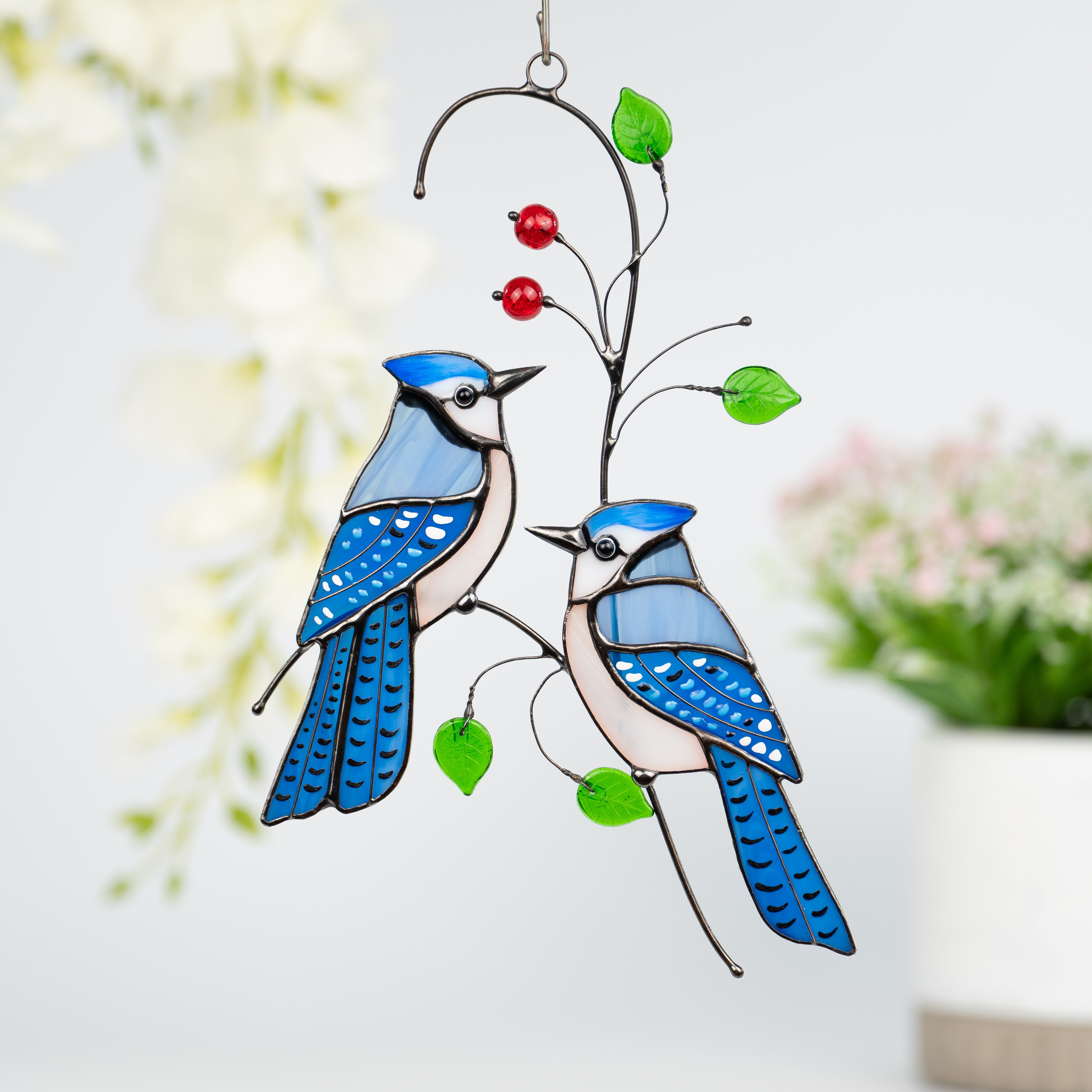 Two stained glass blue jays with red beads and green leaves on wire window hanging
