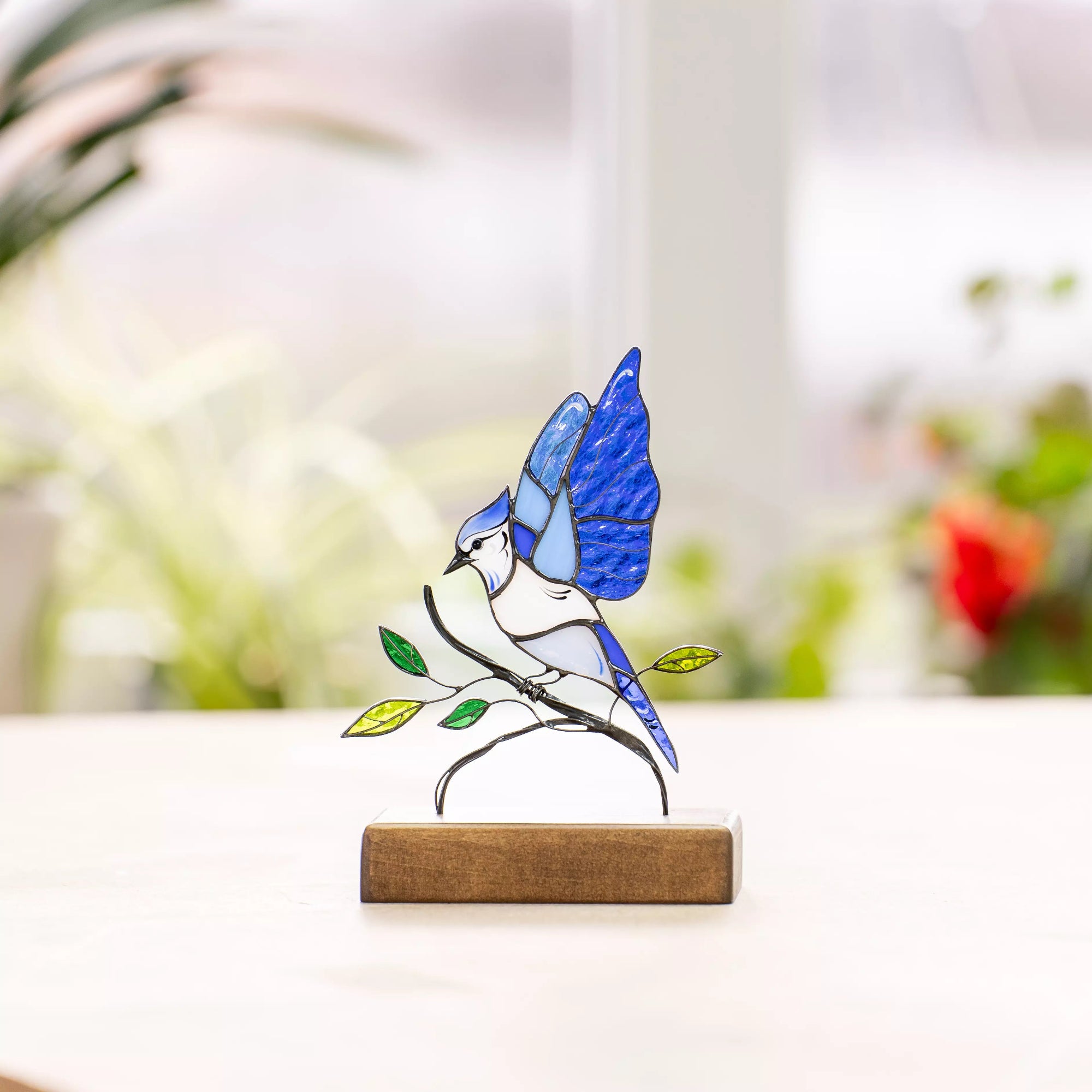 Stained glass blue jay standing on branch with leaves, mounted on wood, placed in bright window light