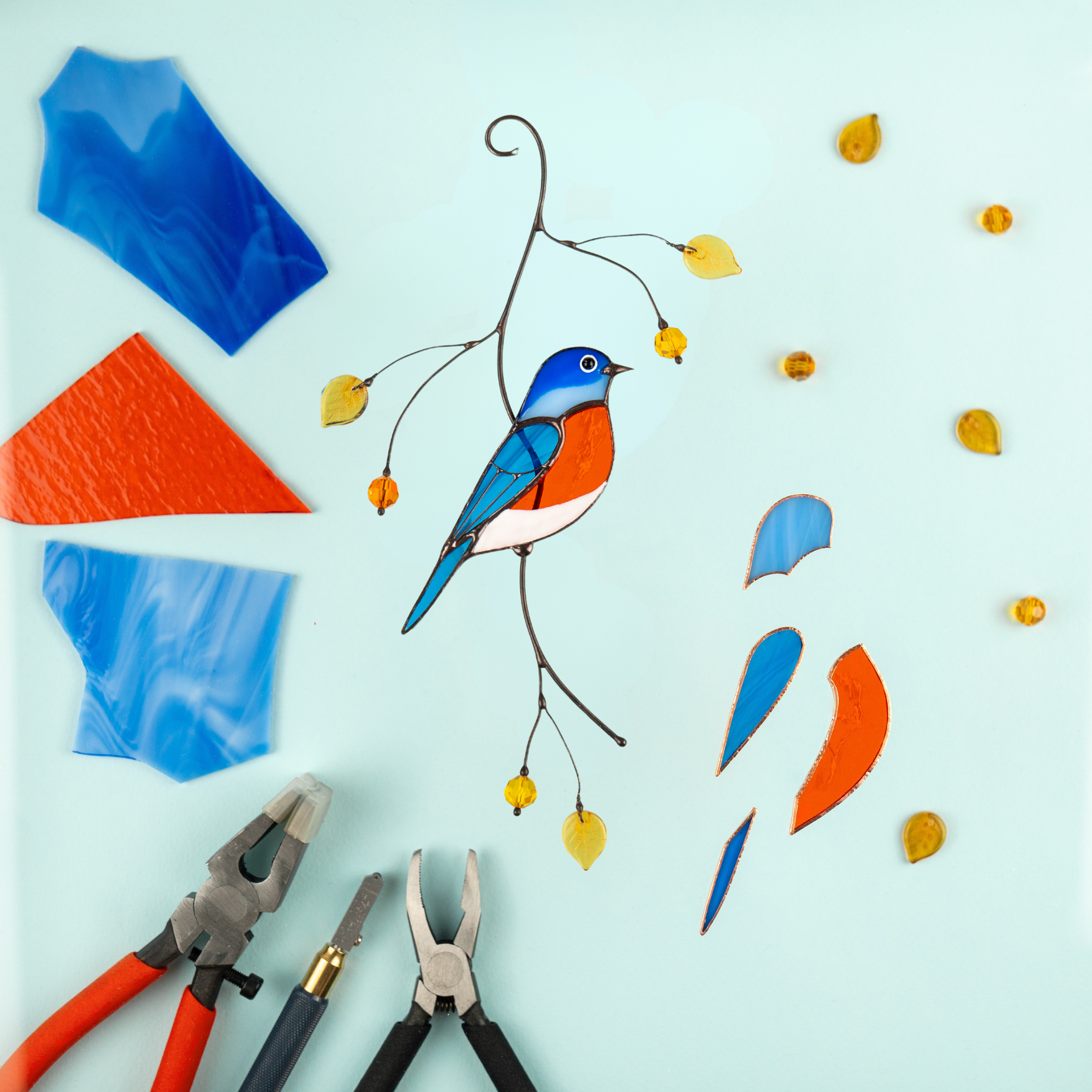 Bluebird suncatcher with tools and colored glass, showcasing the stained glass making process.