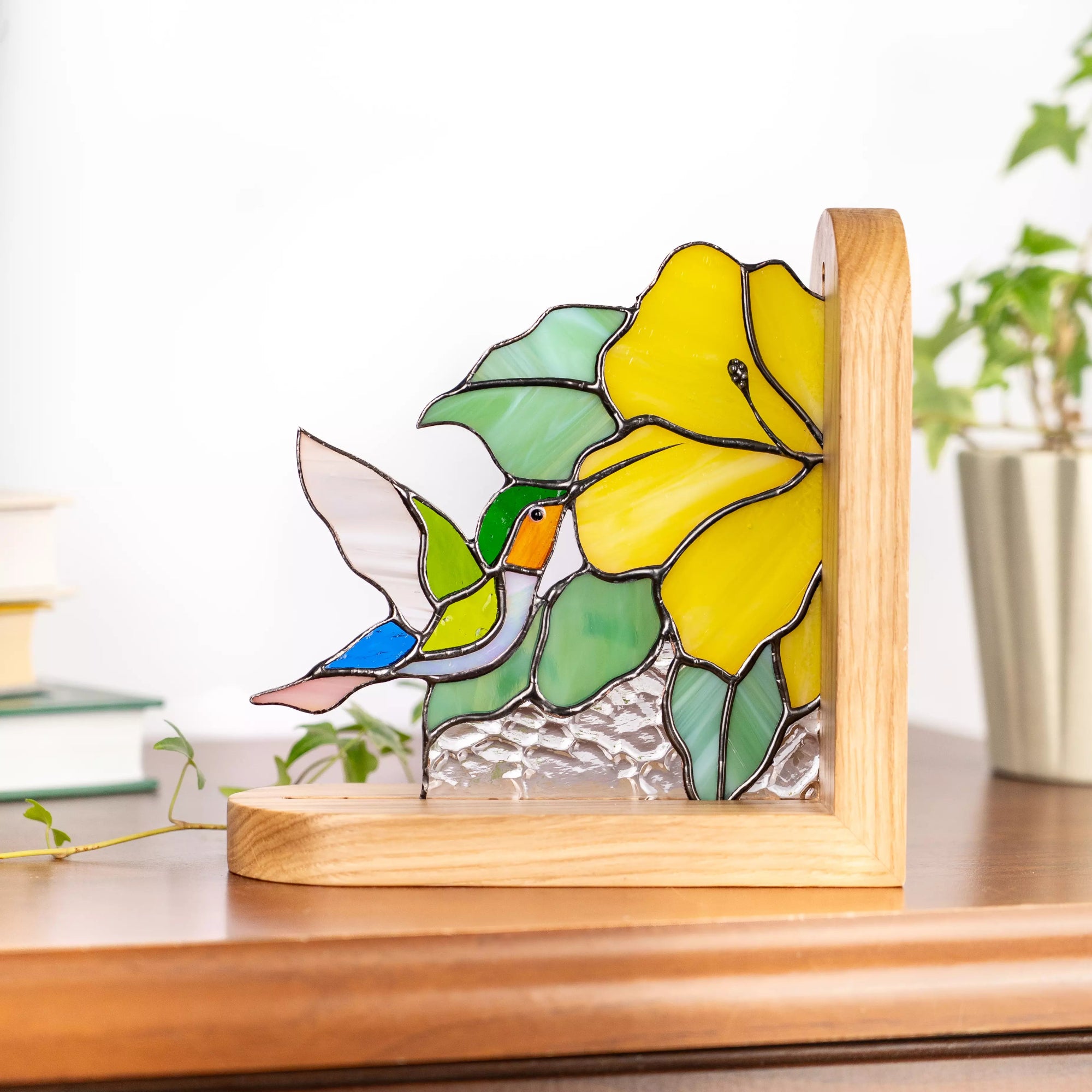Stained glass bookend featuring a hummingbird on a wooden base with a plant in the background