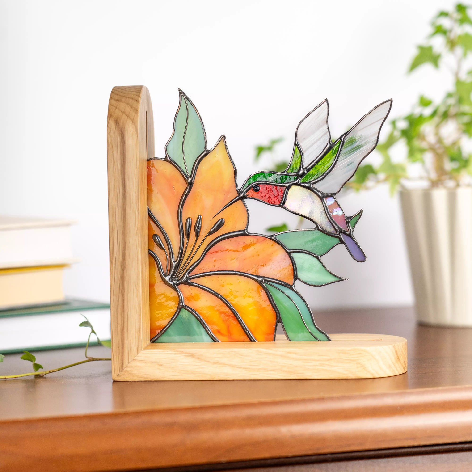Stained glass panel of a hummingbird and flower on a wooden stand with a blurred indoor background.