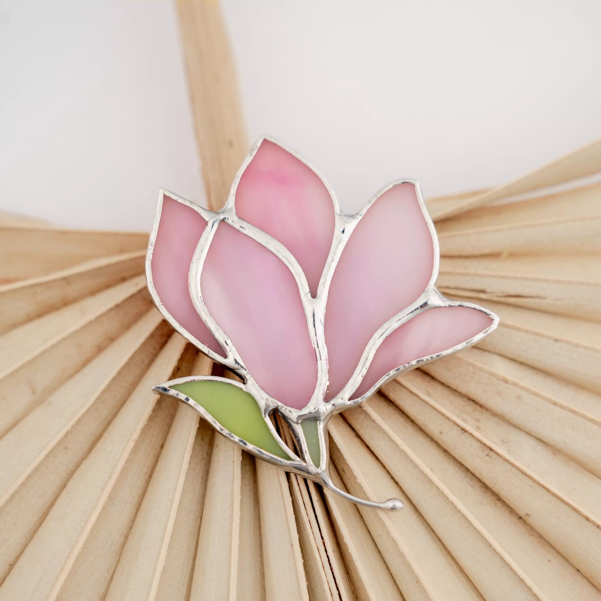 Pink flower-shaped stained glass brooch on a textured beige background