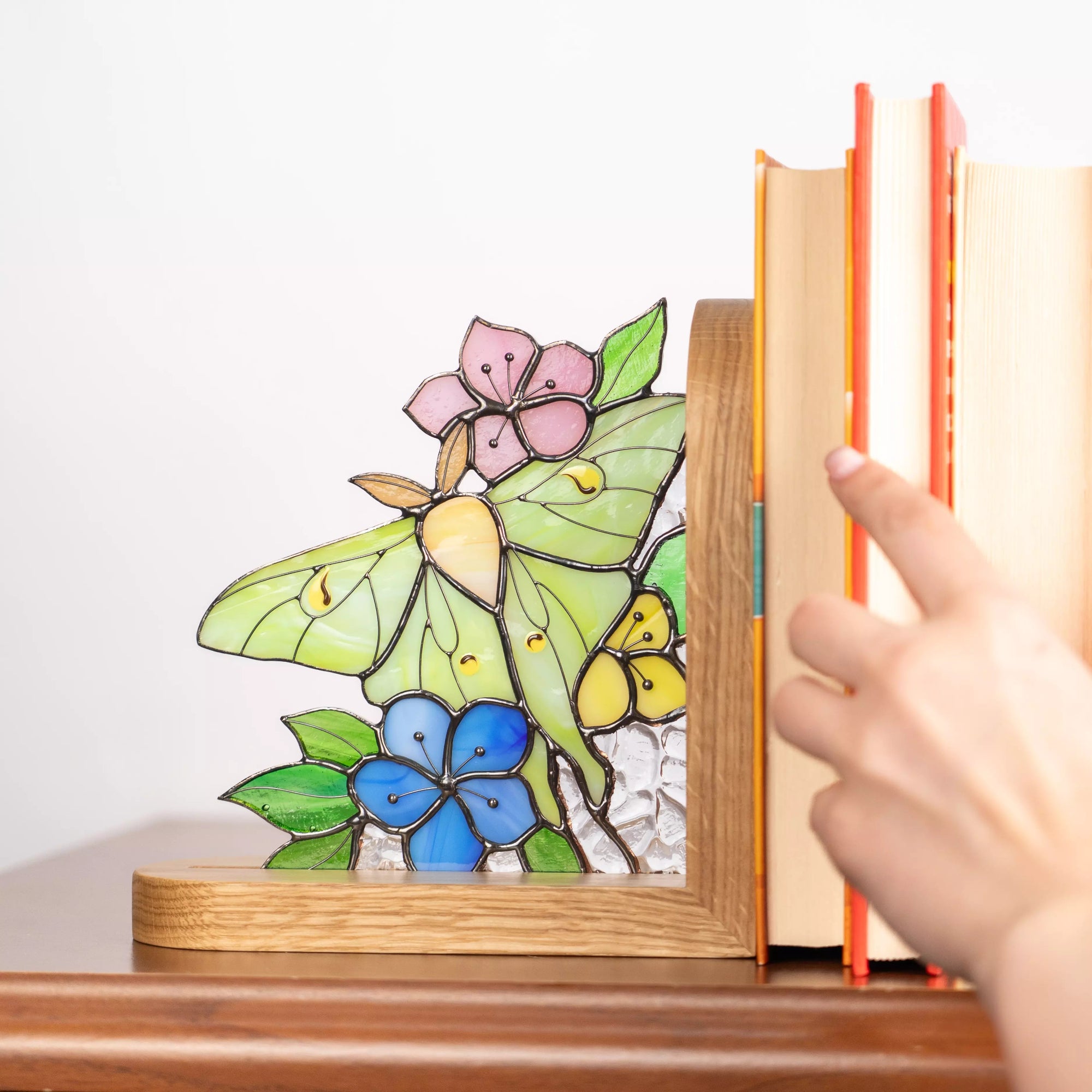Hand pulling books supported by stained glass butterfly bookend with floral design