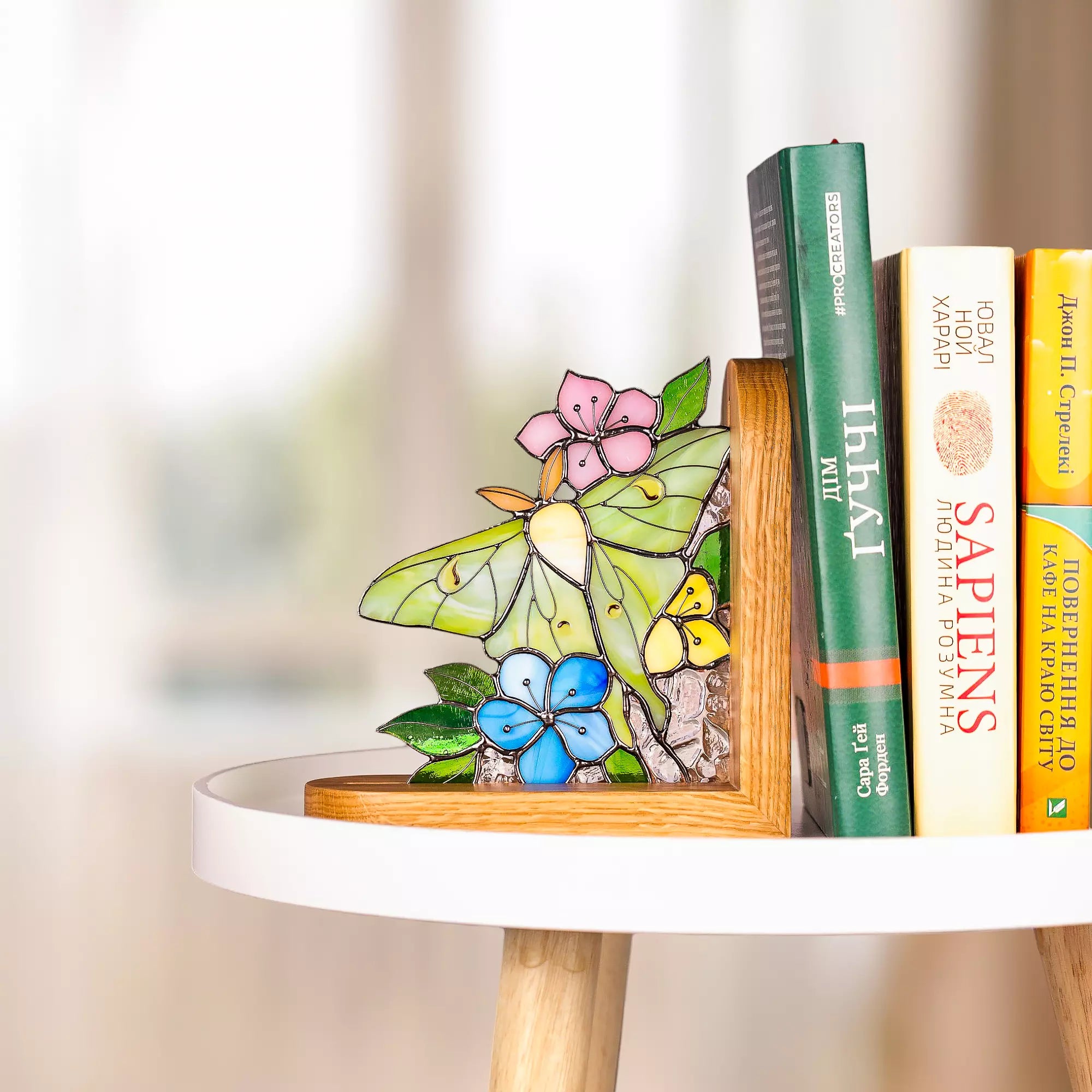 Stained glass luna moth butterfly bookend with flowers placed on a white table in natural daylight