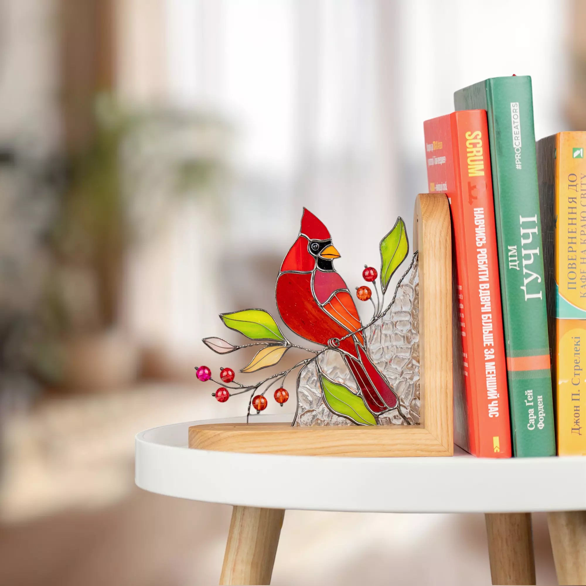 Stained glass cardinal bird bookend displayed on a white side table beside colorful books.