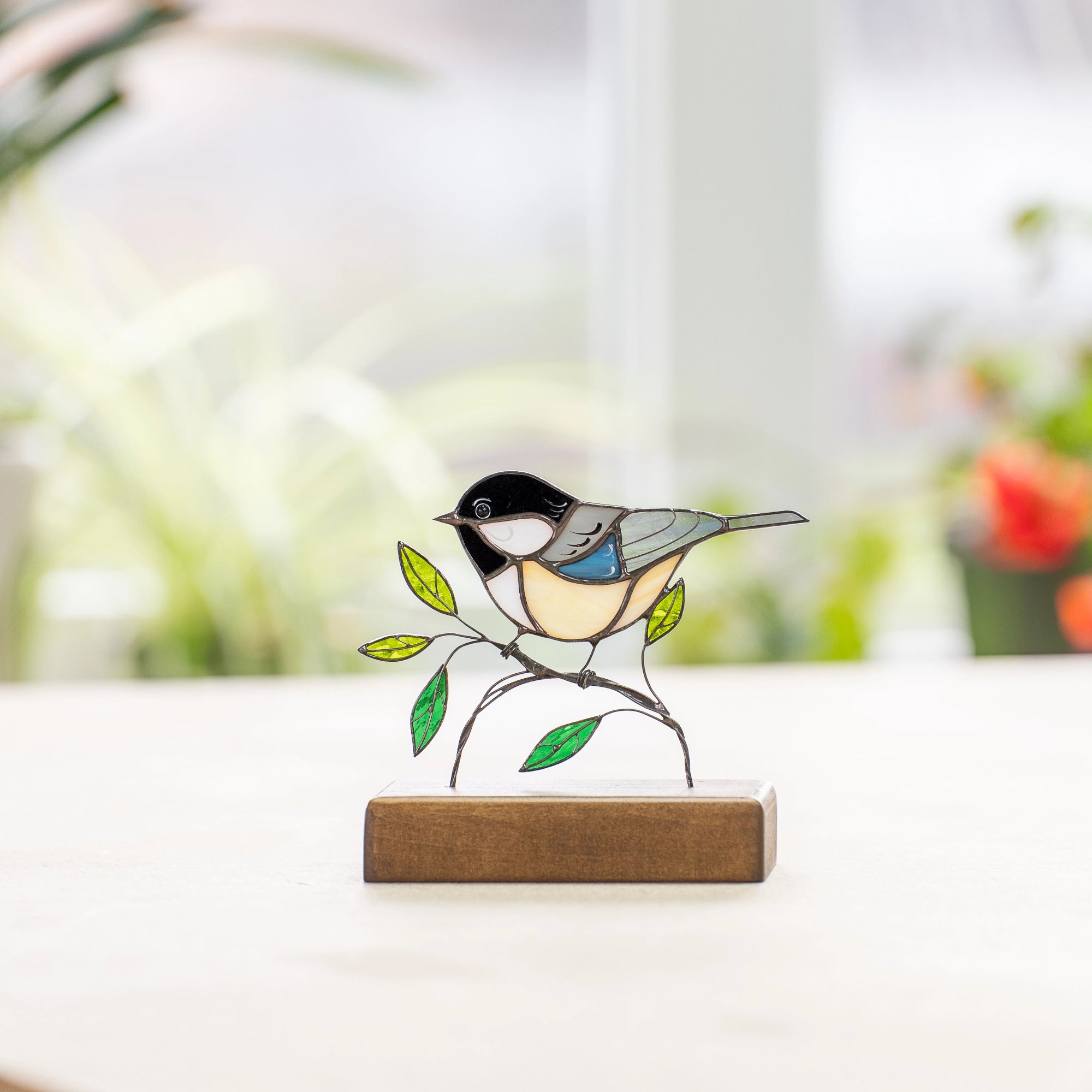 Chickadee stained glass decor on wooden base with green plants in background