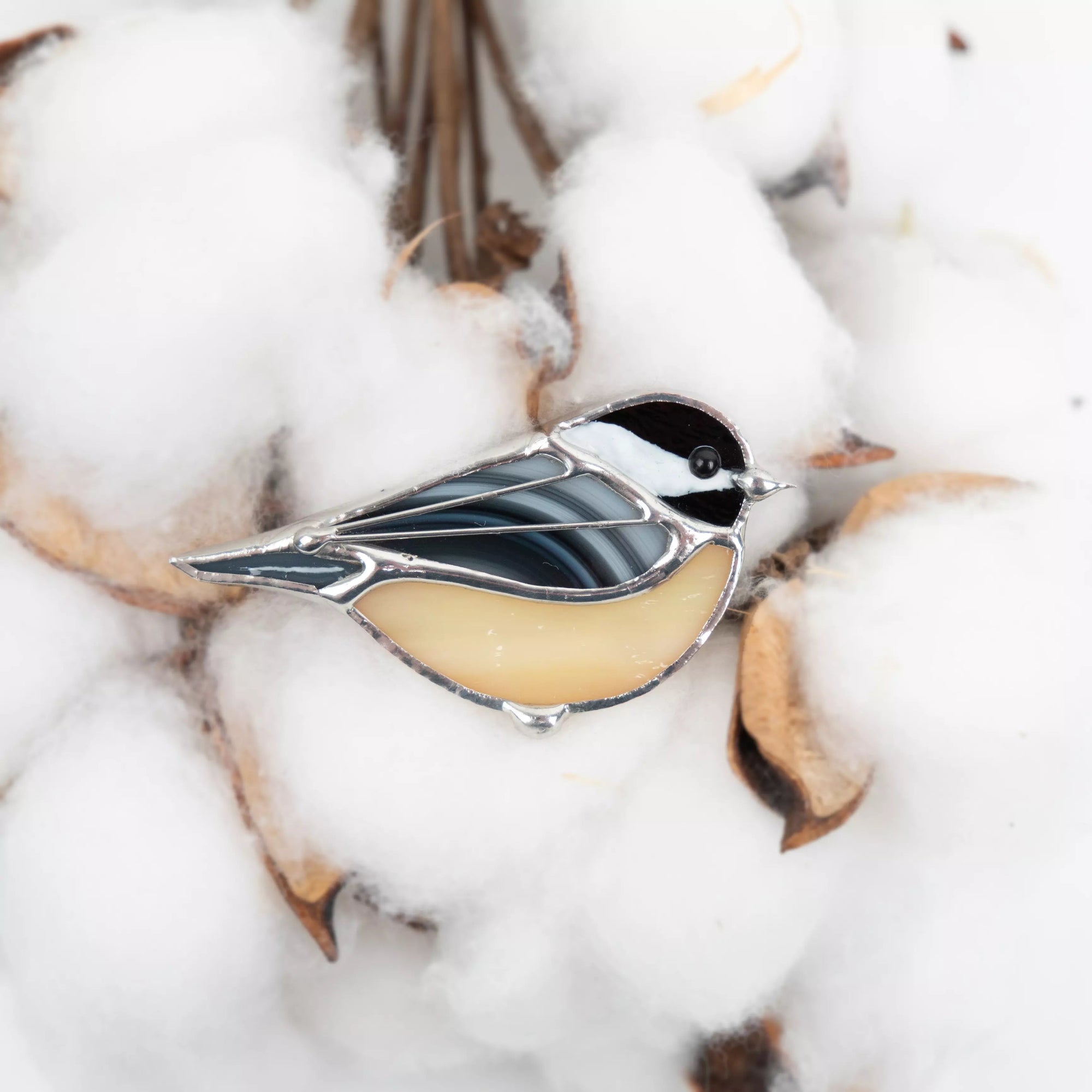 Close-up of chickadee-shaped stained glass brooch placed on white cotton buds.