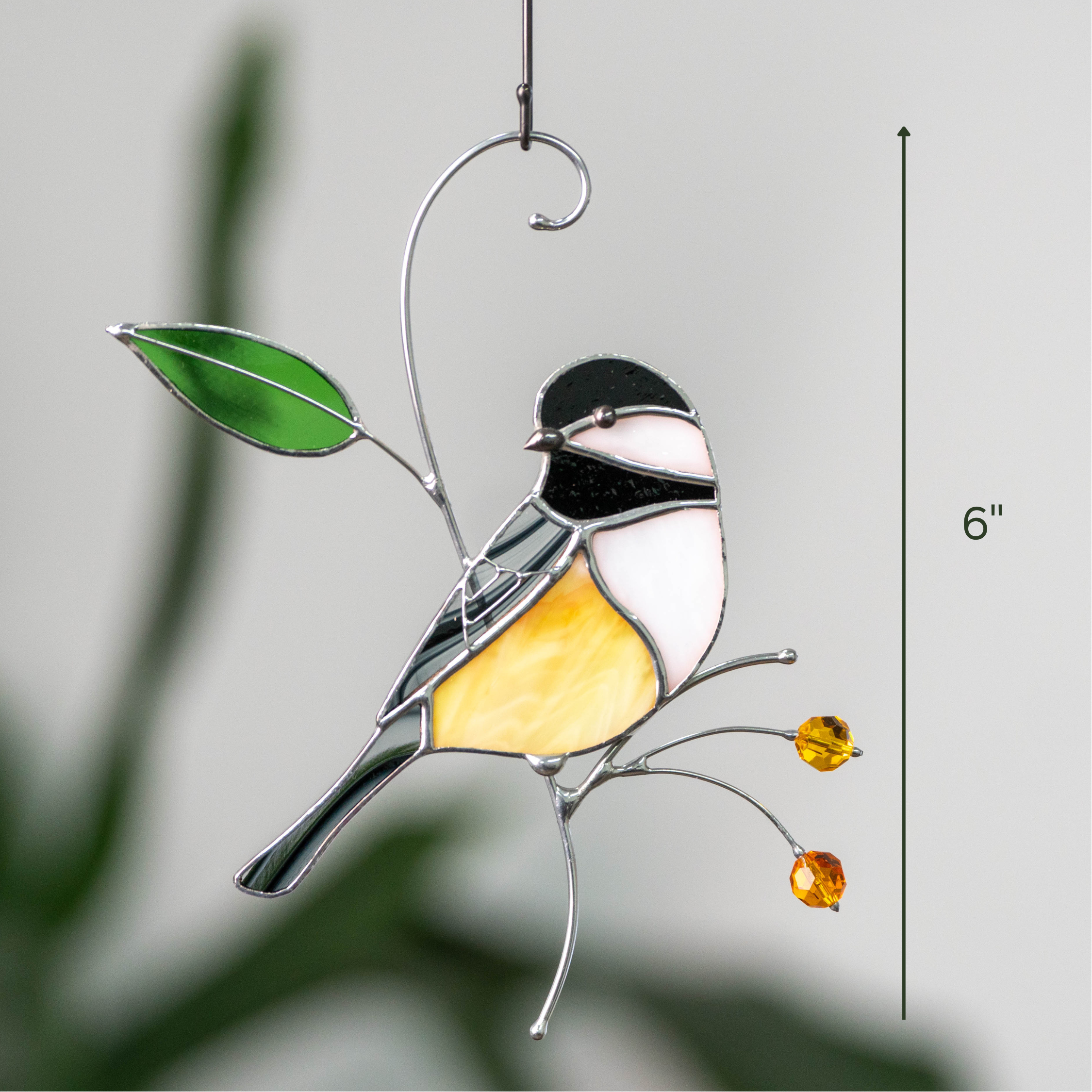 Yellow chickadee suncatcher with black and white head and amber beads hanging from a hook, plant background and 6” label.