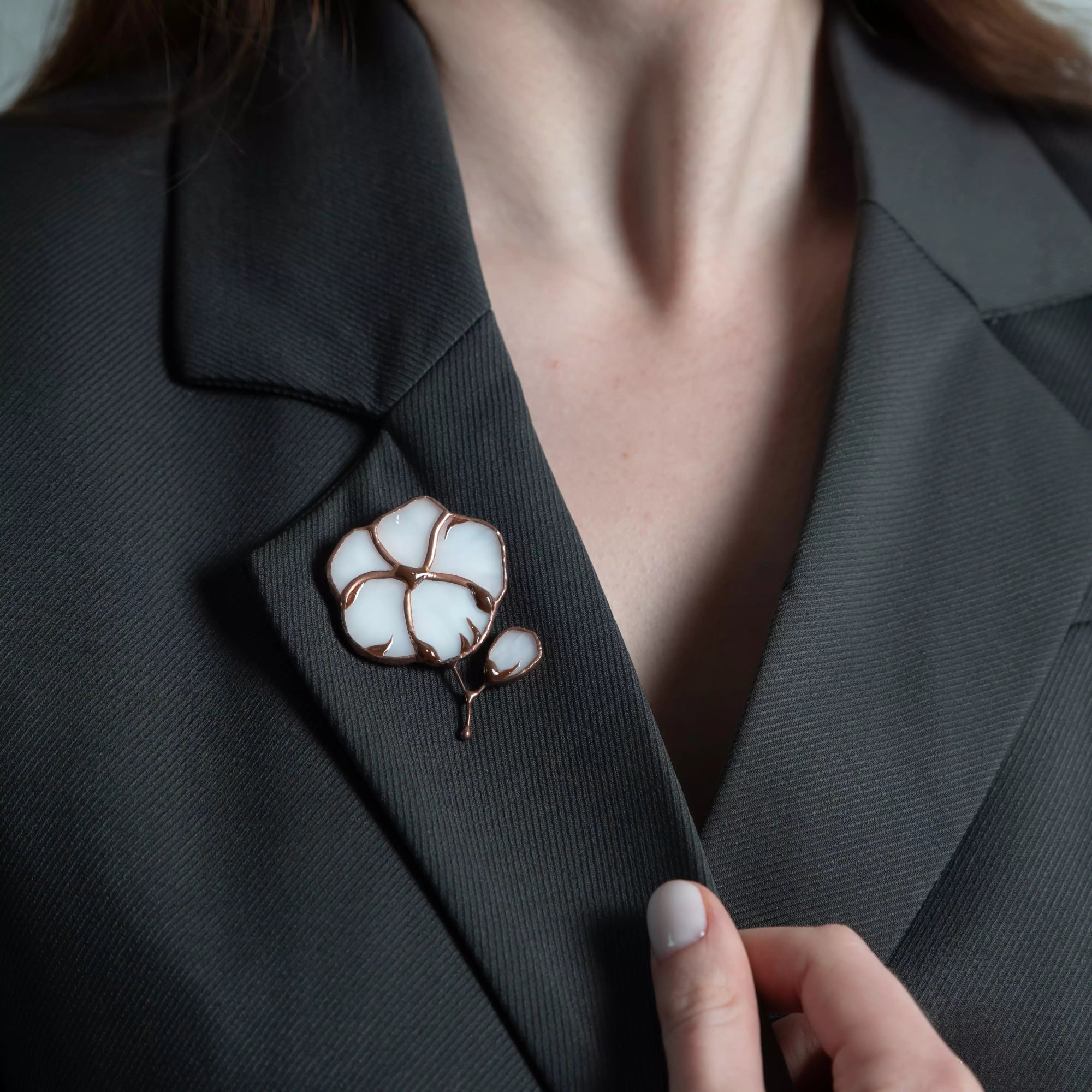 A white and brown cotton flower brooch in stained glass pinned to a dark jacket, adding elegant accent.
