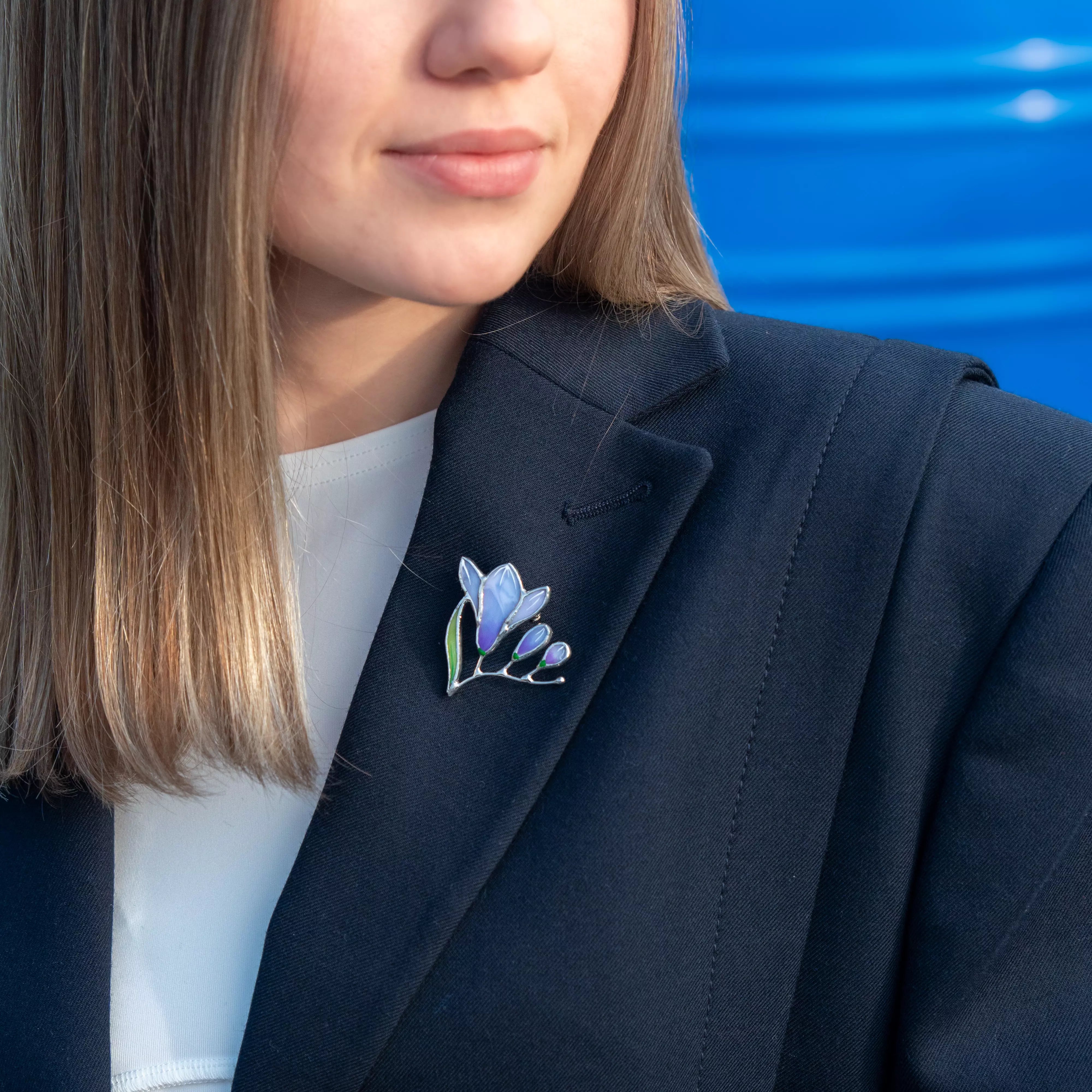 Woman wearing a dark blazer with a stained glass brooch of a purple freesia on the lapel
