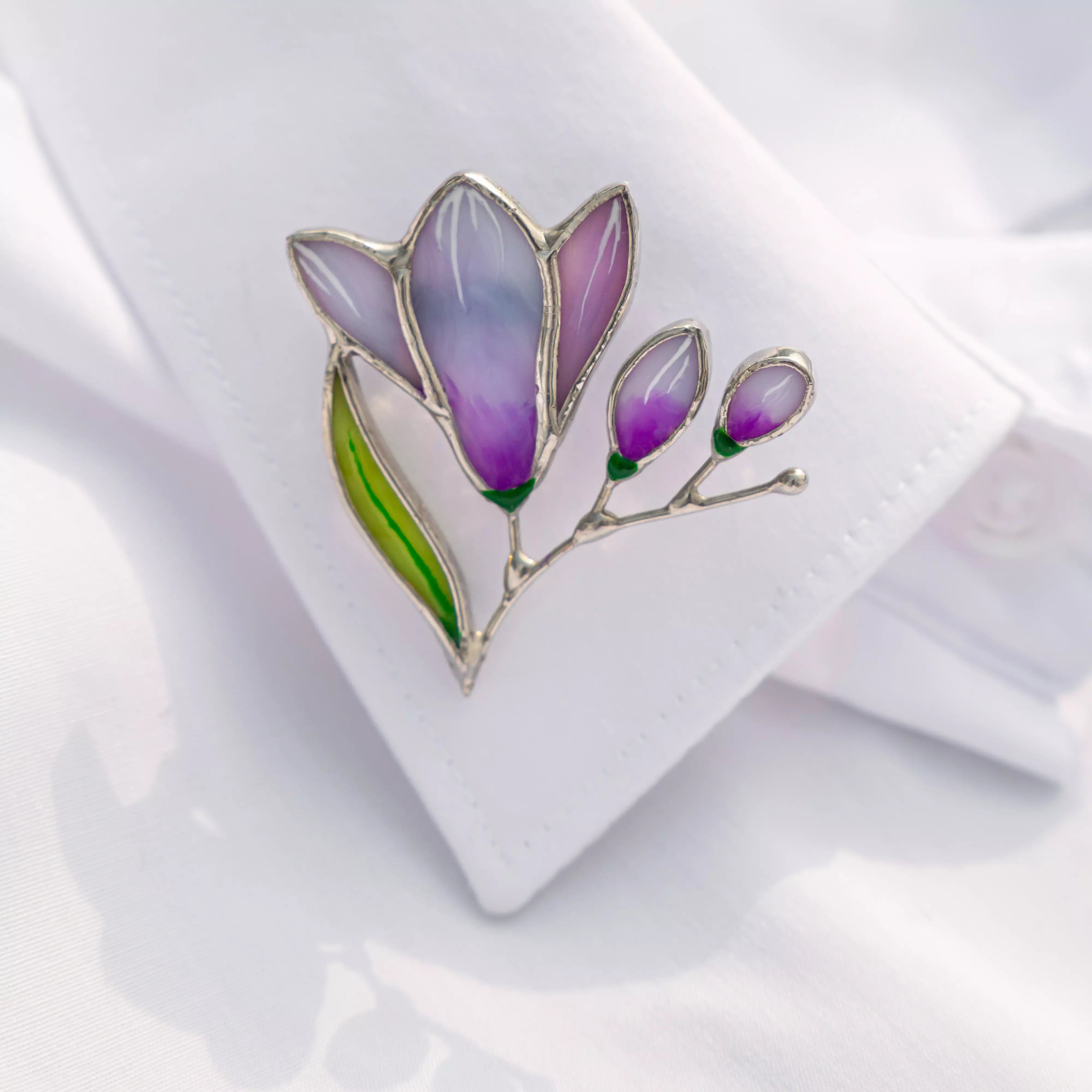 Close-up of a purple free-shaped stained glass brooch pinned to the cuff of a white shirtia