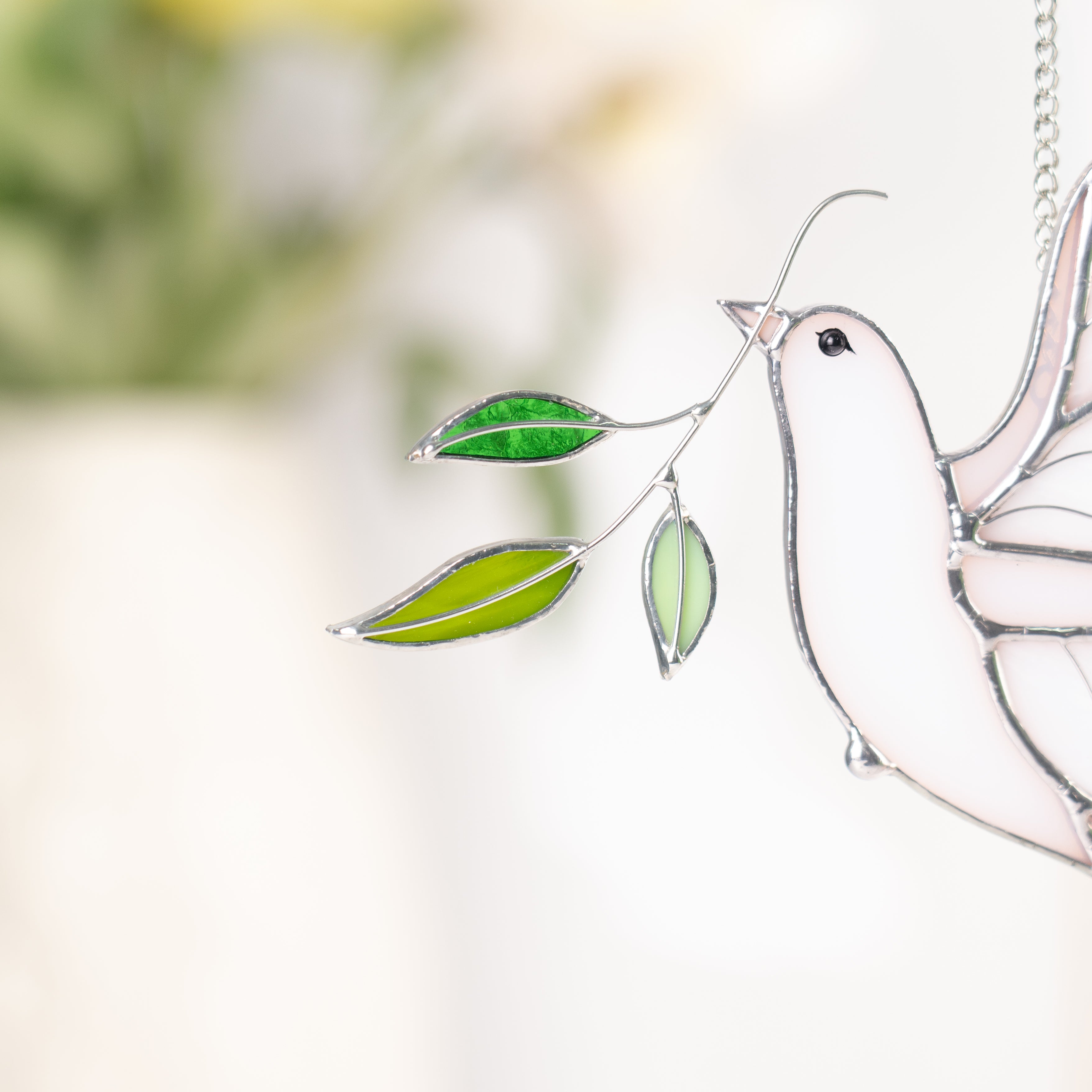 White stained glass dove with green leaves against a blurred background