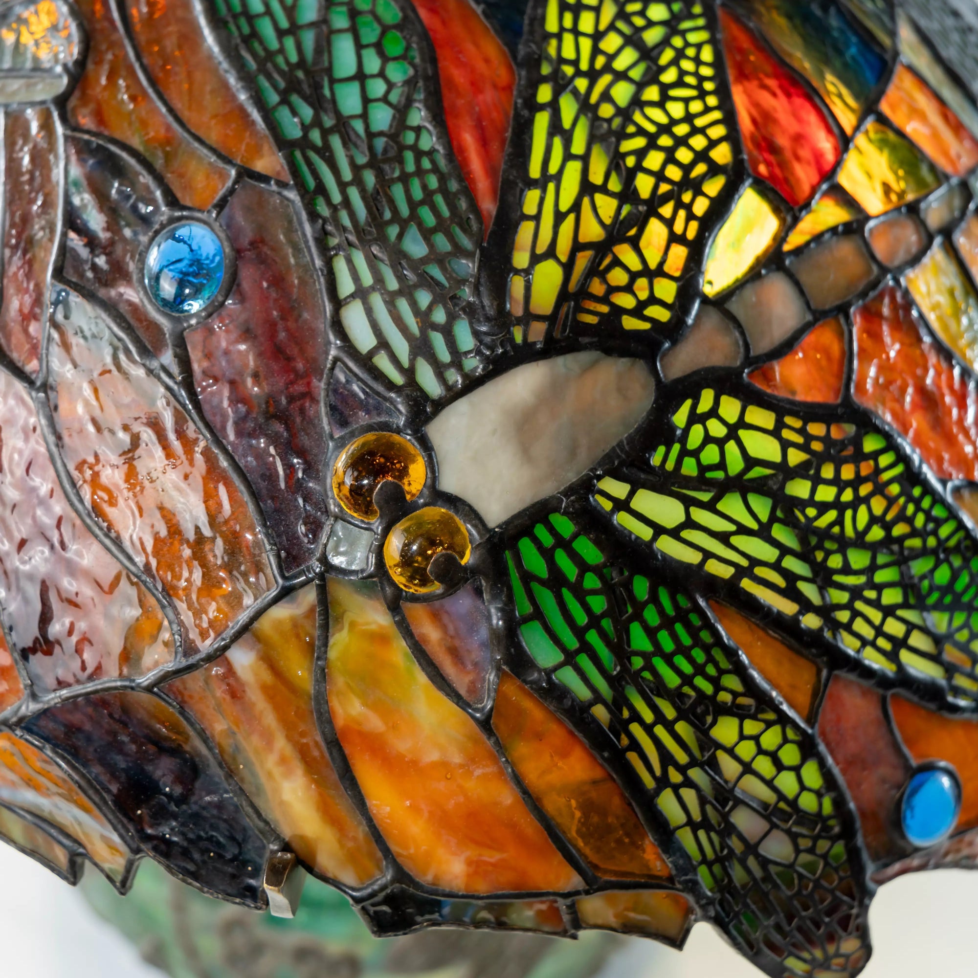 Close-up of stained glass lamp with dragonfly wings in green and amber tones on a curved glass dome