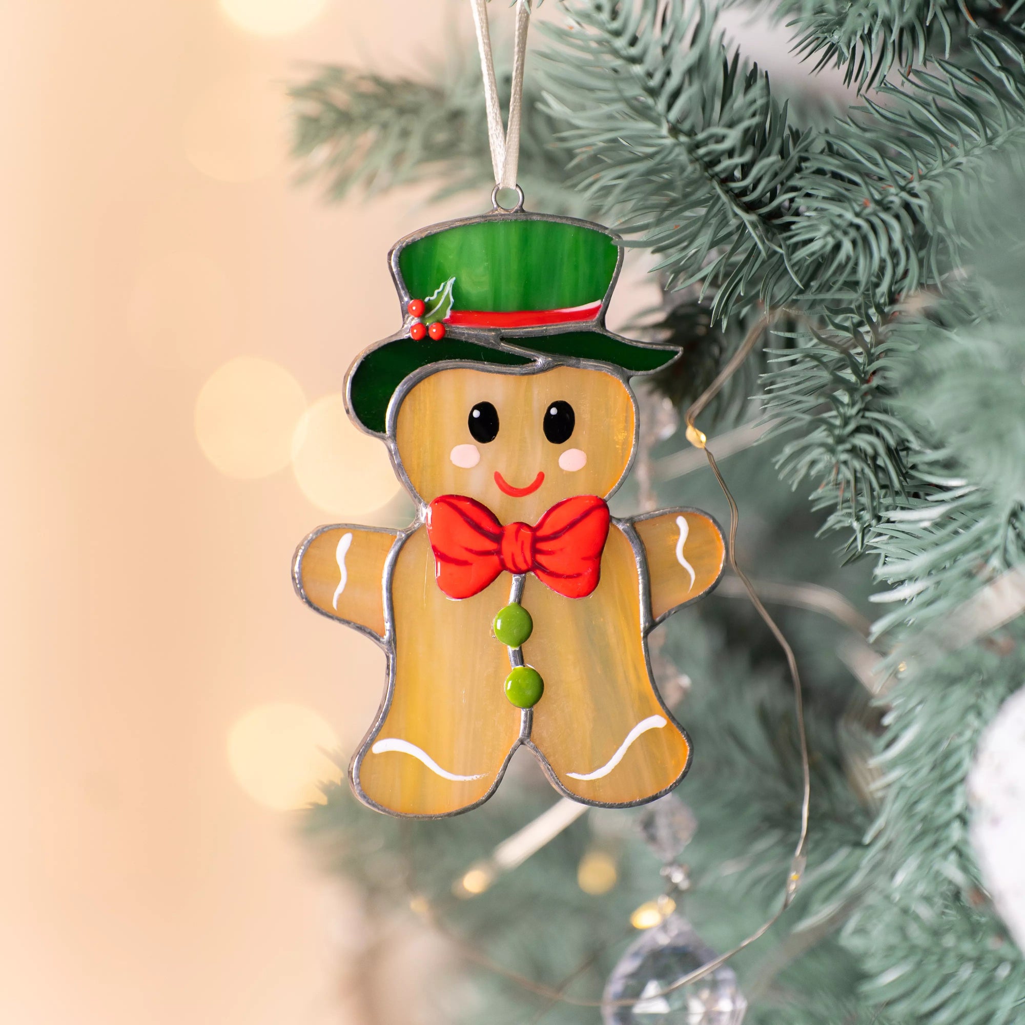 Close-up of gingerbread man stained glass ornament hanging on a Christmas tree with warm bokeh lights.