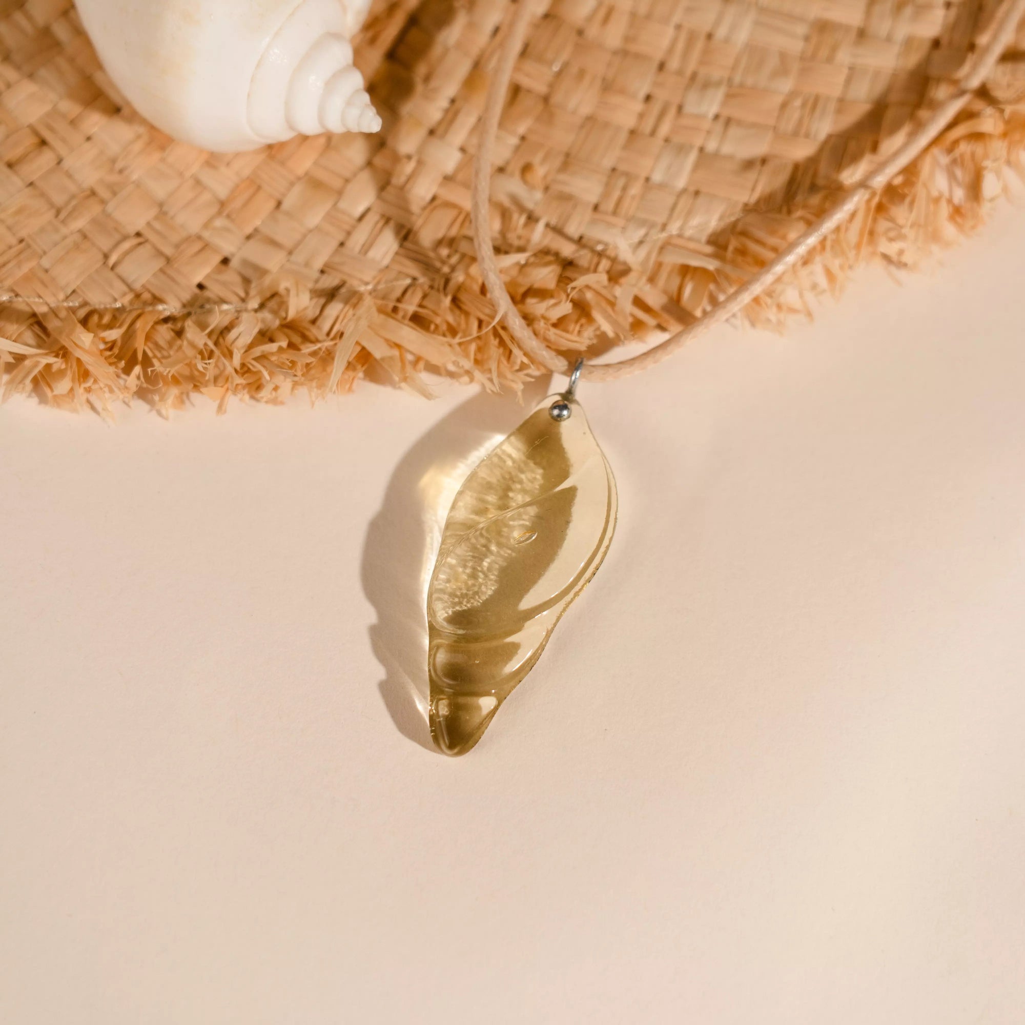 Golden colored pendant on a beige surface with a woven mat and shell in the background