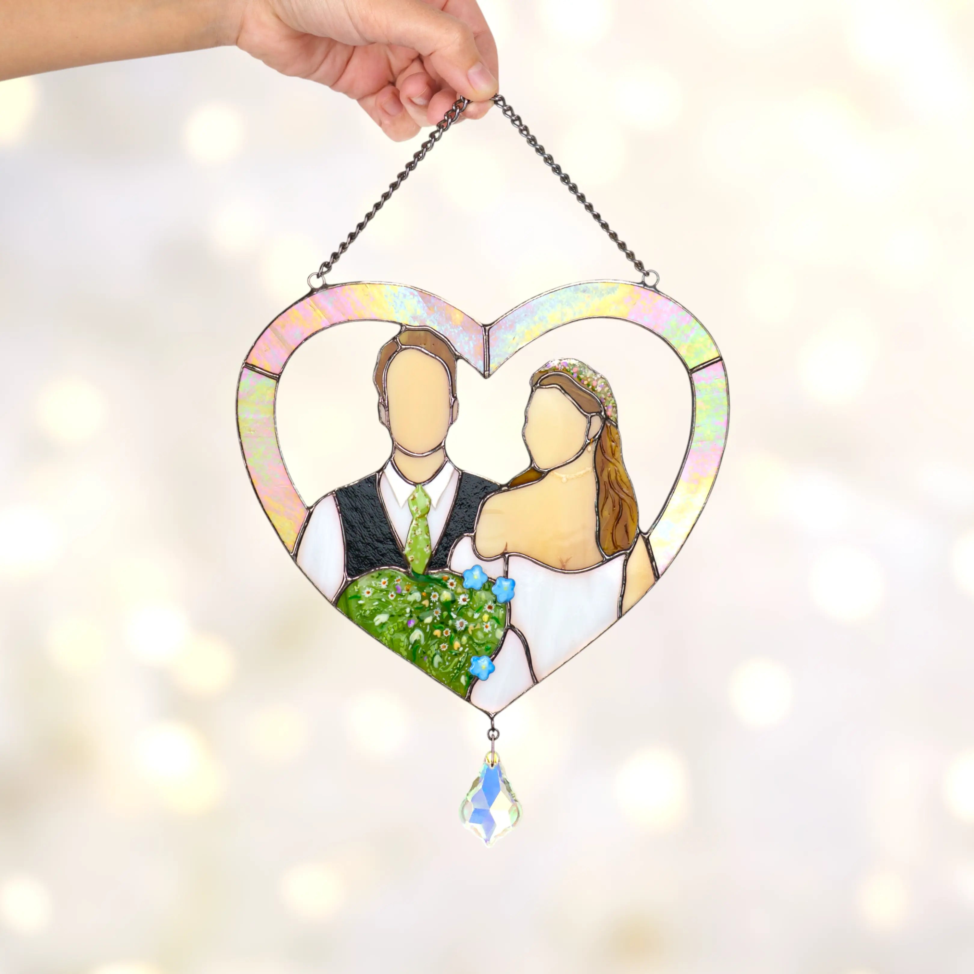 Heart-shaped stained glass panel with a couple, held by a hand against a light background.