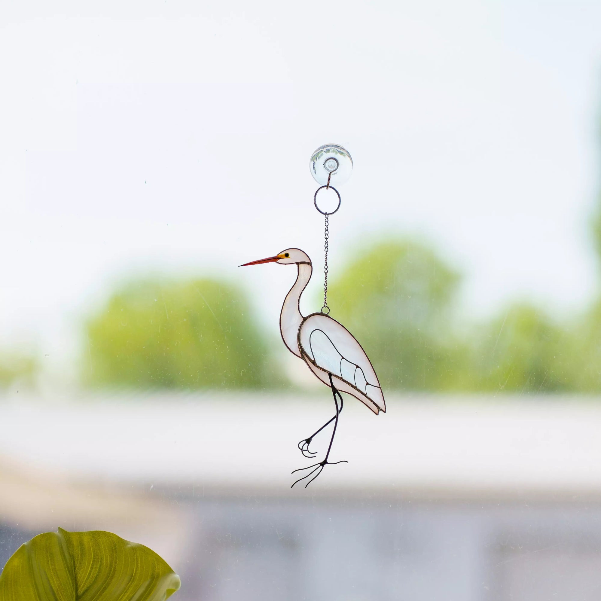 Stained glass white heron window hanging with a blurred green outdoor background