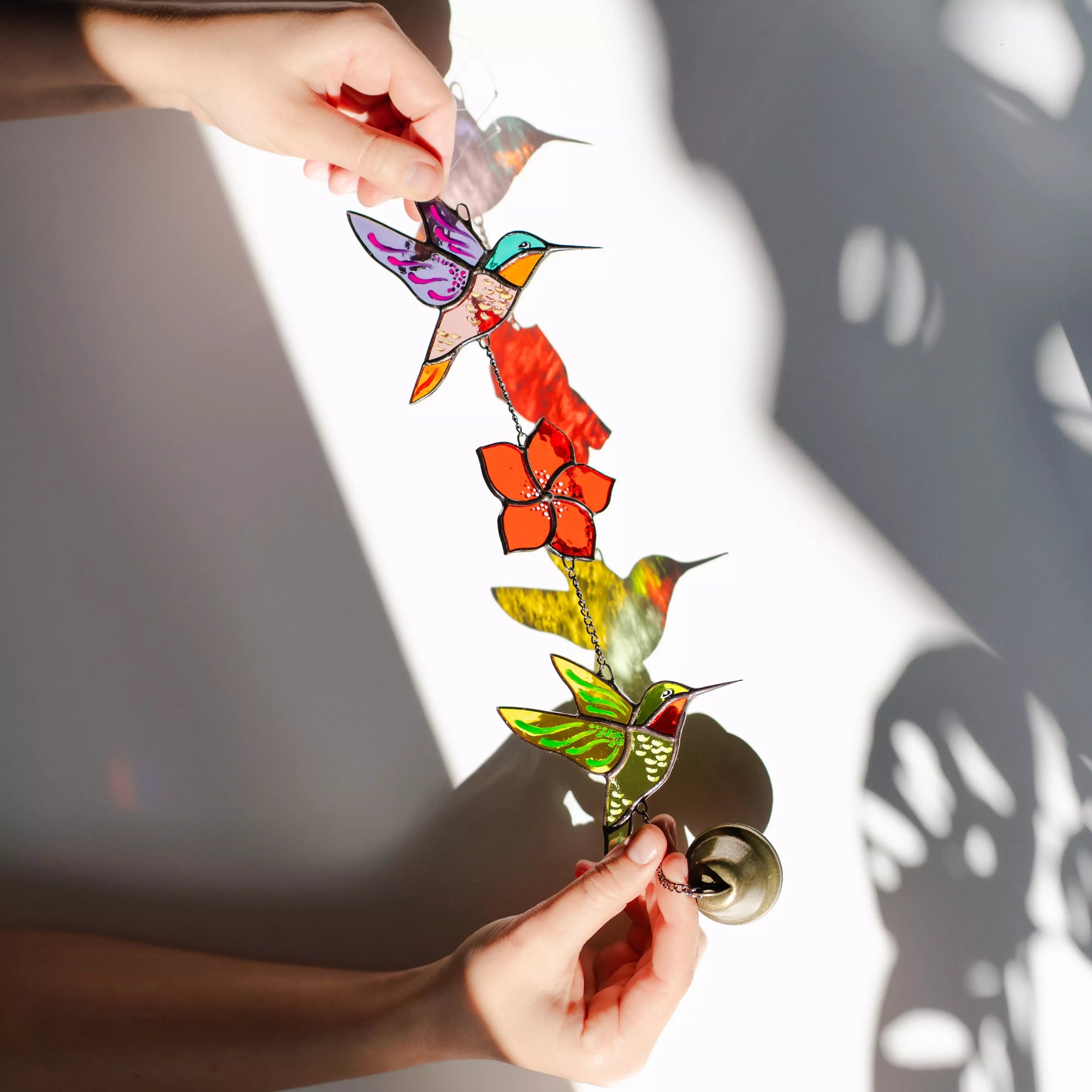 Colorful stained glass hummingbird and flower decoration held by hands against a light background
