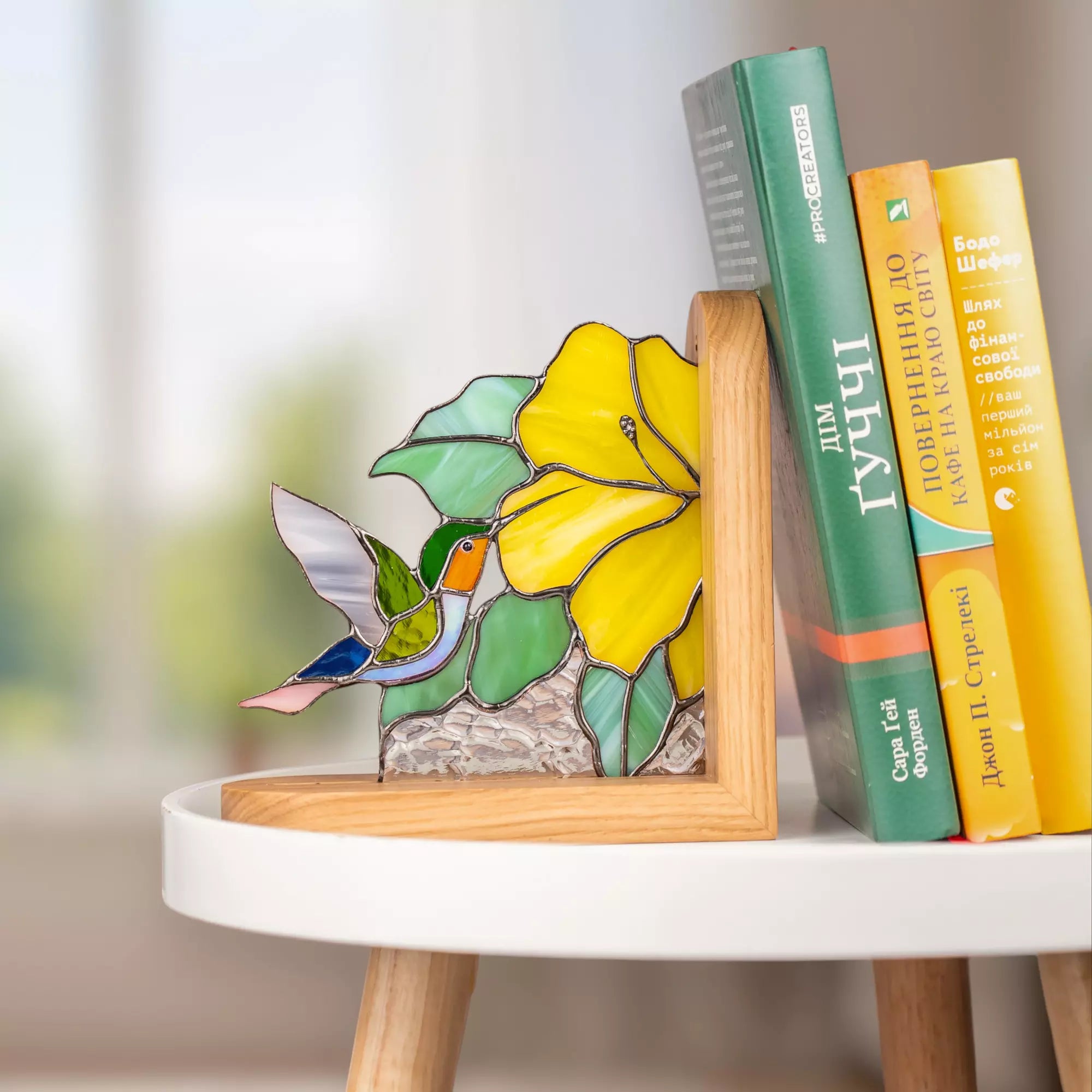 Stained glass bookend with hummingbird and yellow flower next to books on a round table