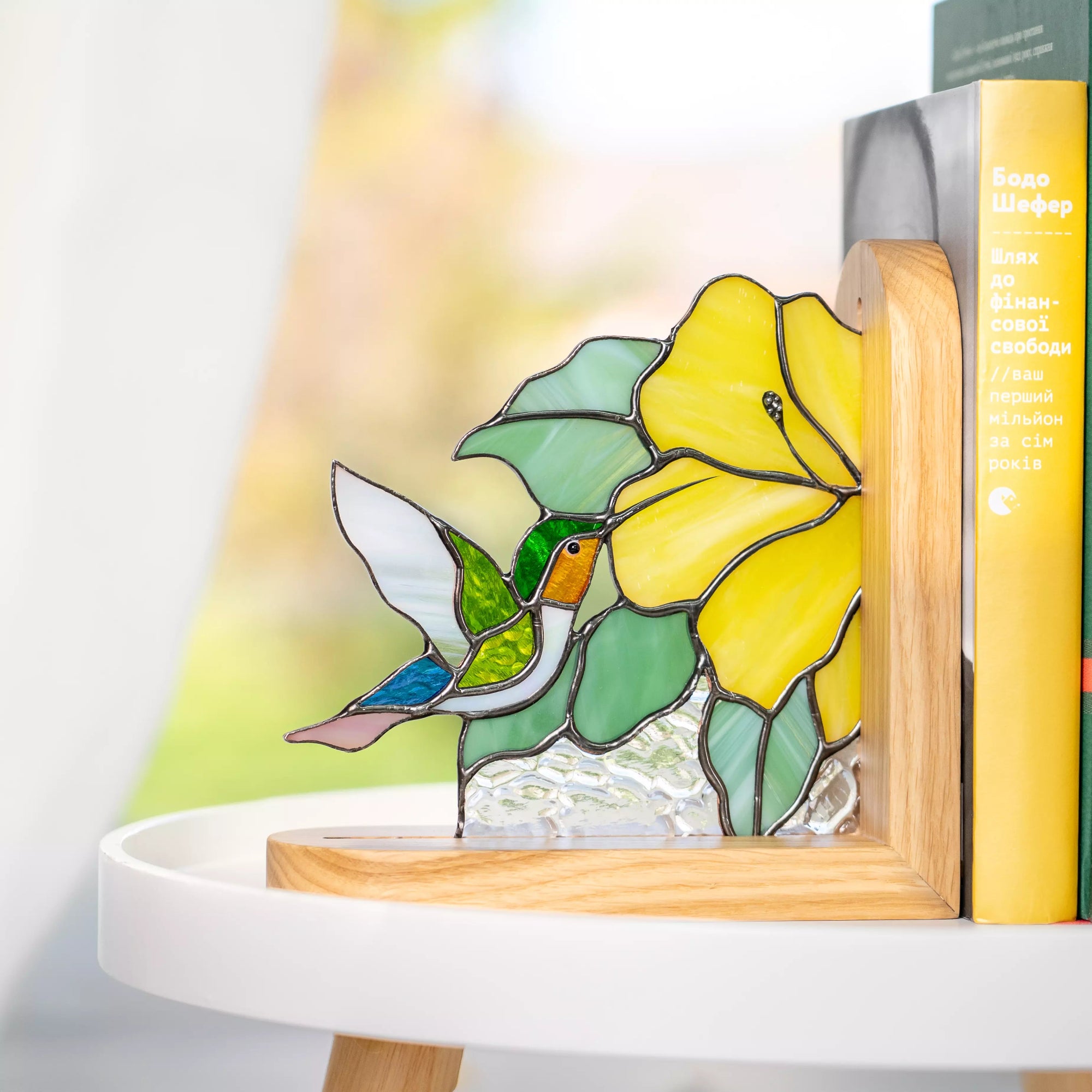 Stained glass bookend hummingbird flying toward a yellow flower, bookend decor on a shelf with books