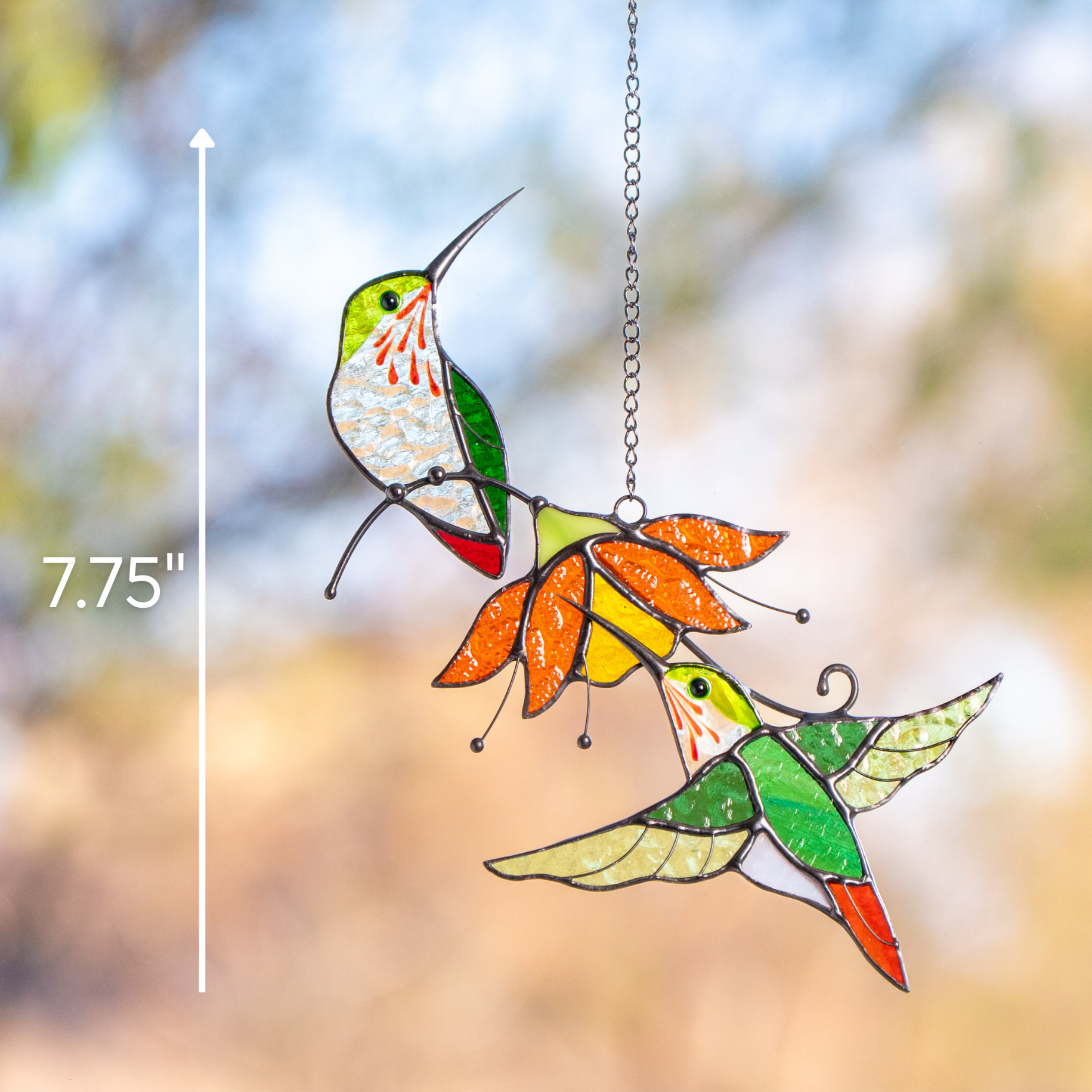 Suncatcher of two hummingbirds and orange flower hanging in window with 7.75" size marked on the photo.