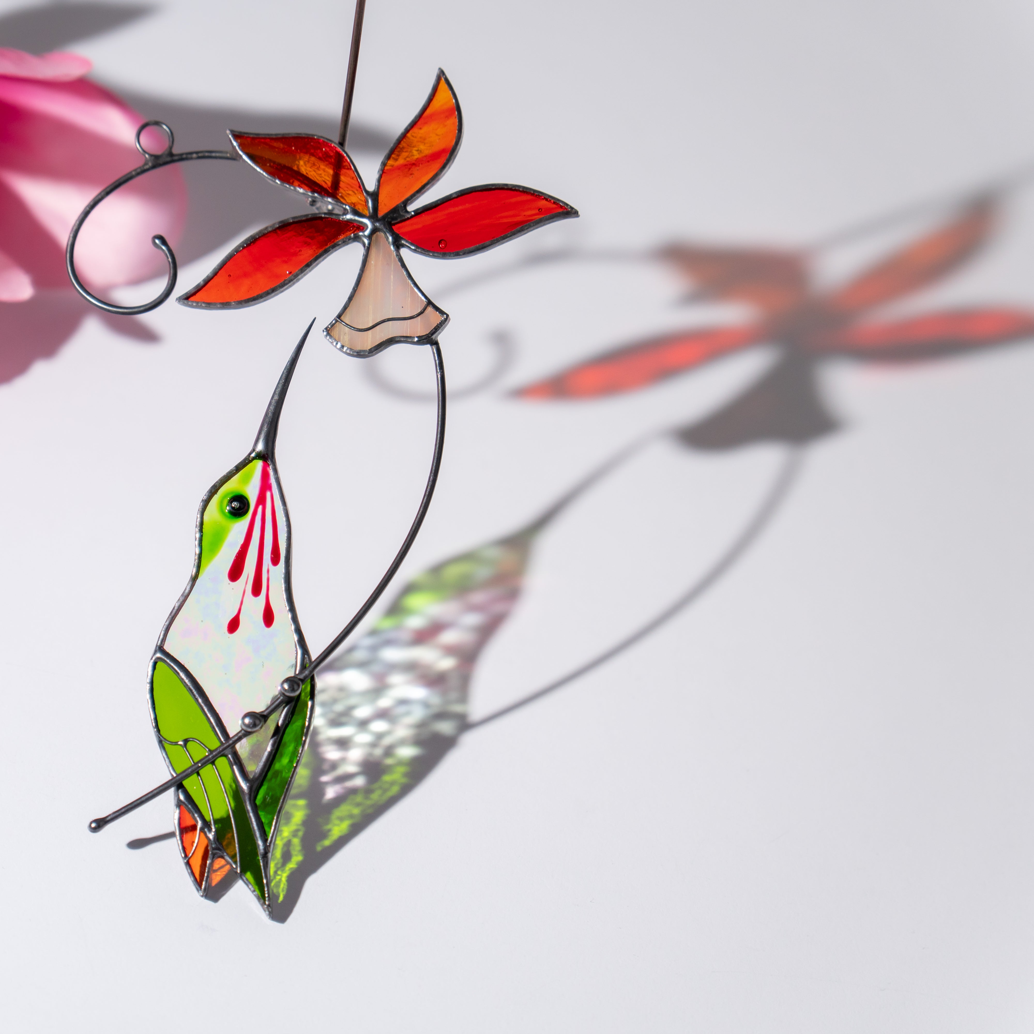 Hummingbird and red bell flower suncatcher creating bright colored shadows under sunlight.