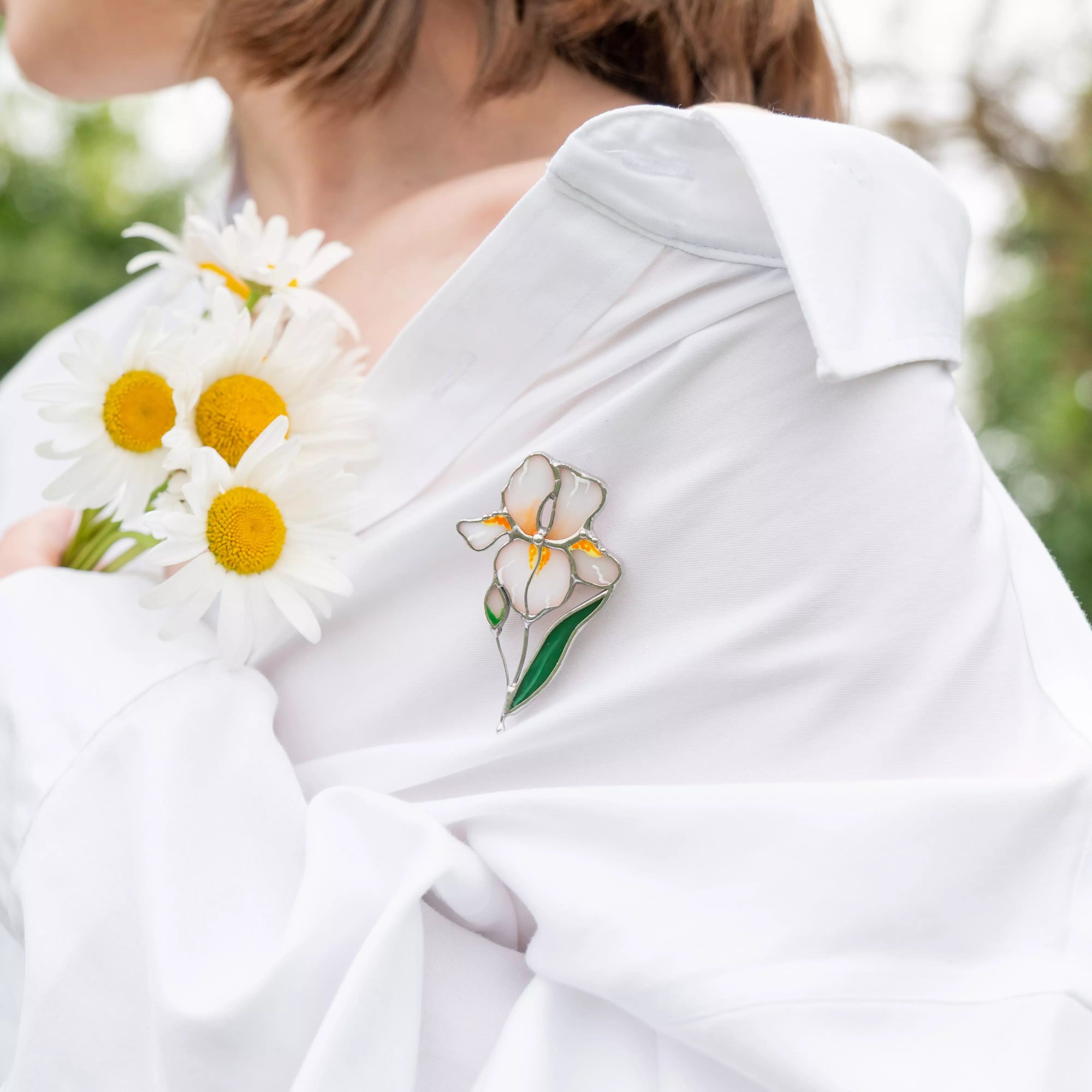 Person wearing a white shirt with white iris brooch, holding flowers.
