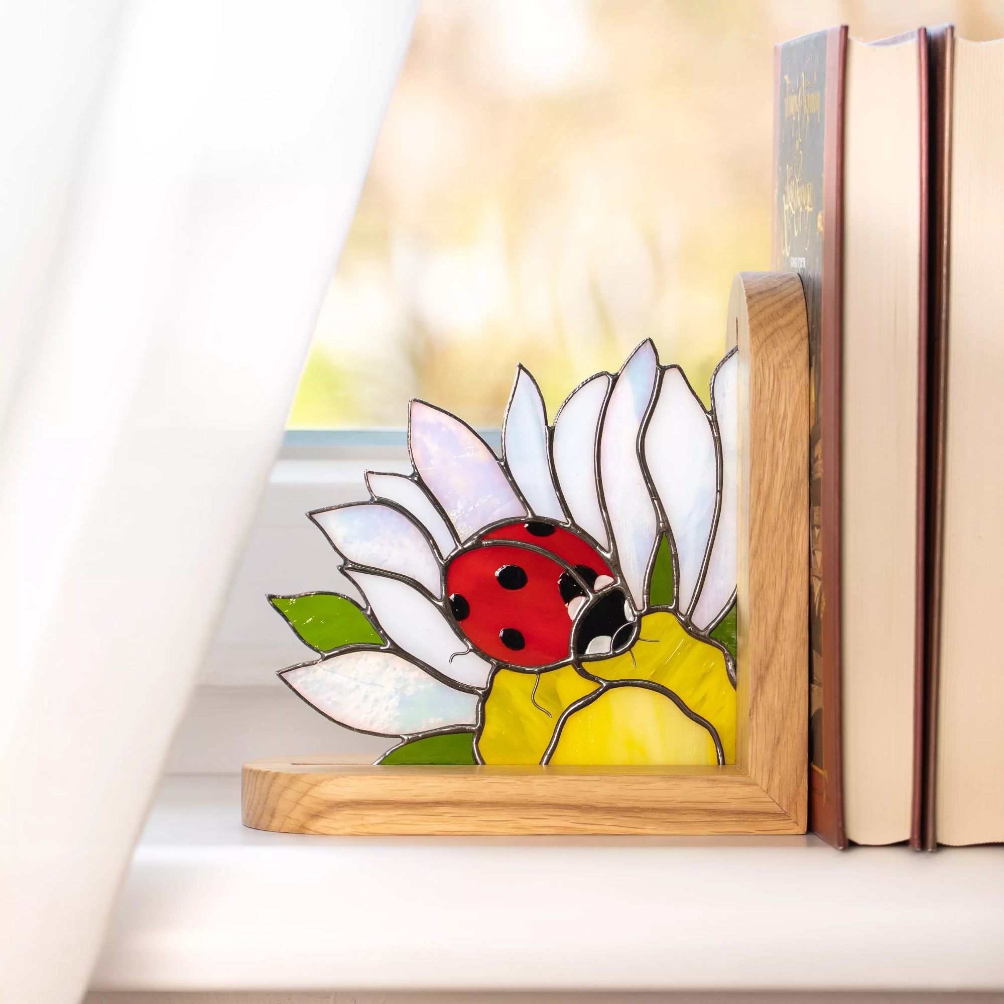 Handcrafted stained glass ladybug sitting on a white daisy flower. The petals feature an iridescent pearl finish, and the bright red beetle adds a pop of color to the wooden bookend base.