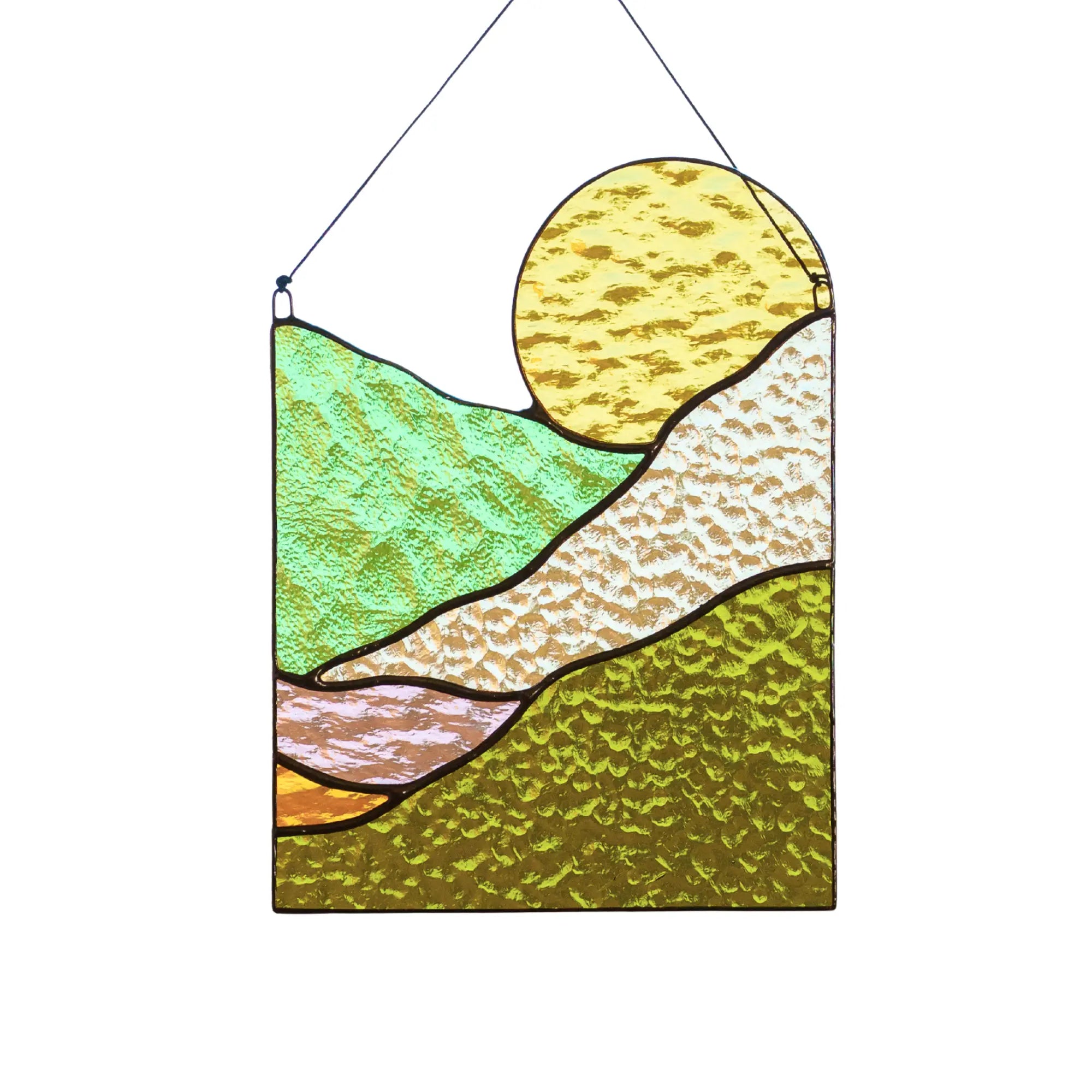 A rectangular stained glass suncatcher featuring a large yellow sun rising over rolling green and amber hills.