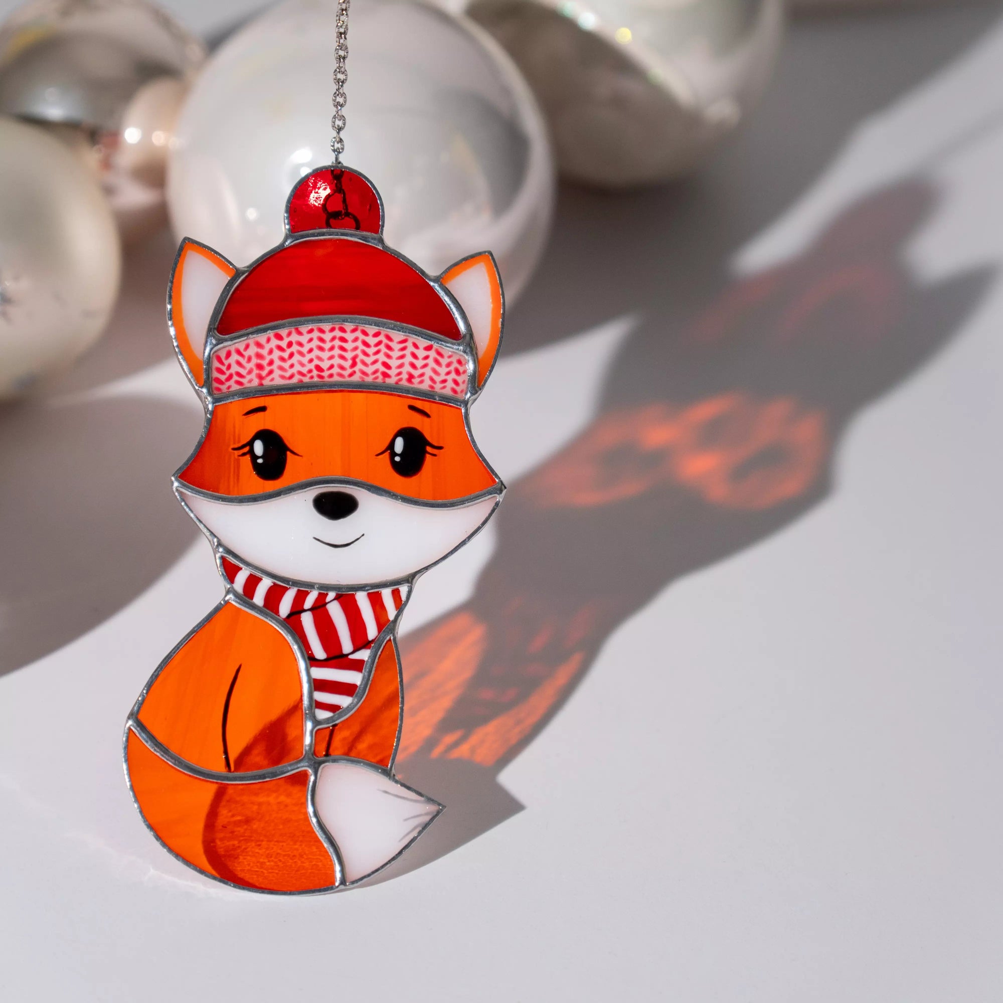 Stained glass window hanging fox wearing a red hat and scarf on a light background