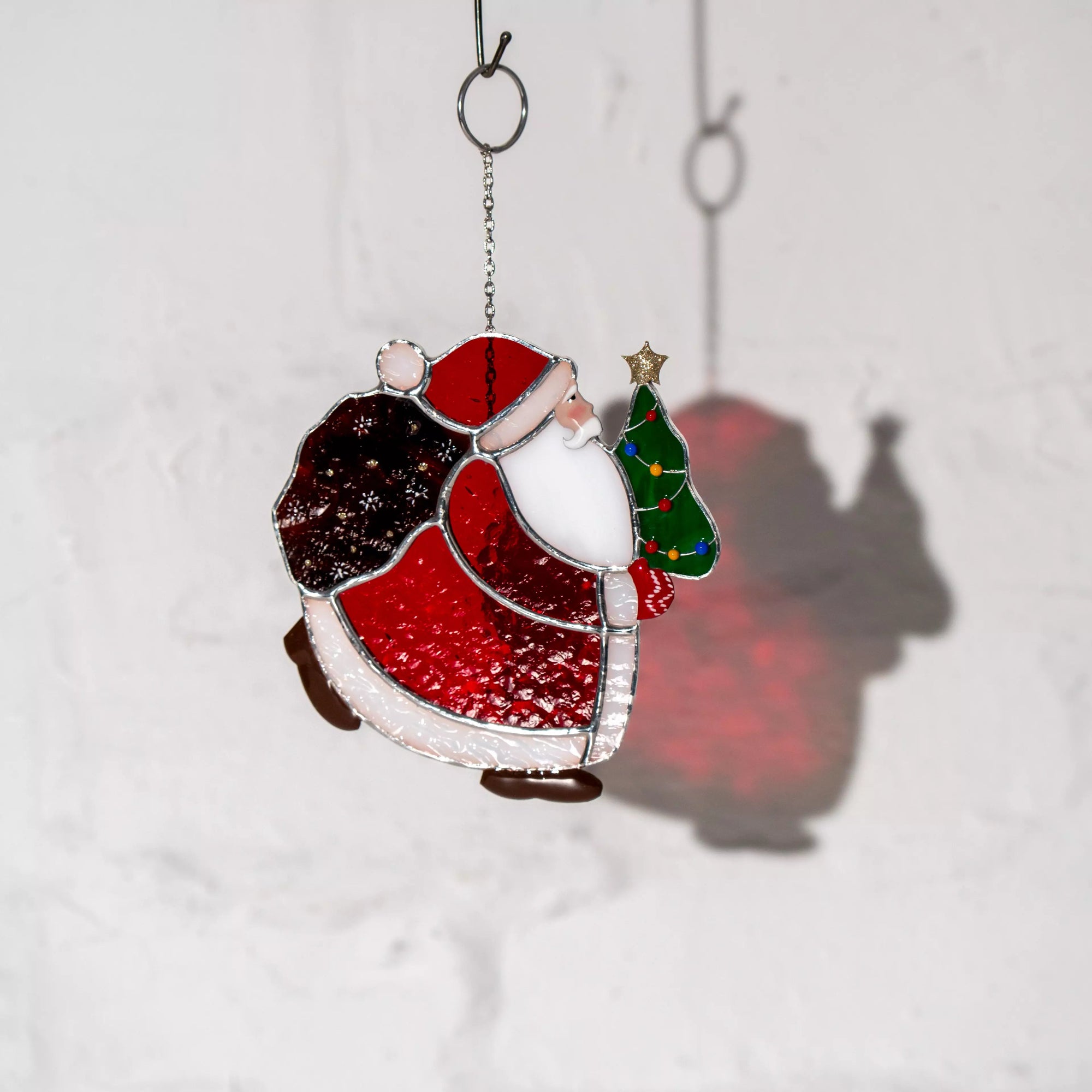 Stained glass window hanging of a Santa Claus holding a Christmas tree on a white background