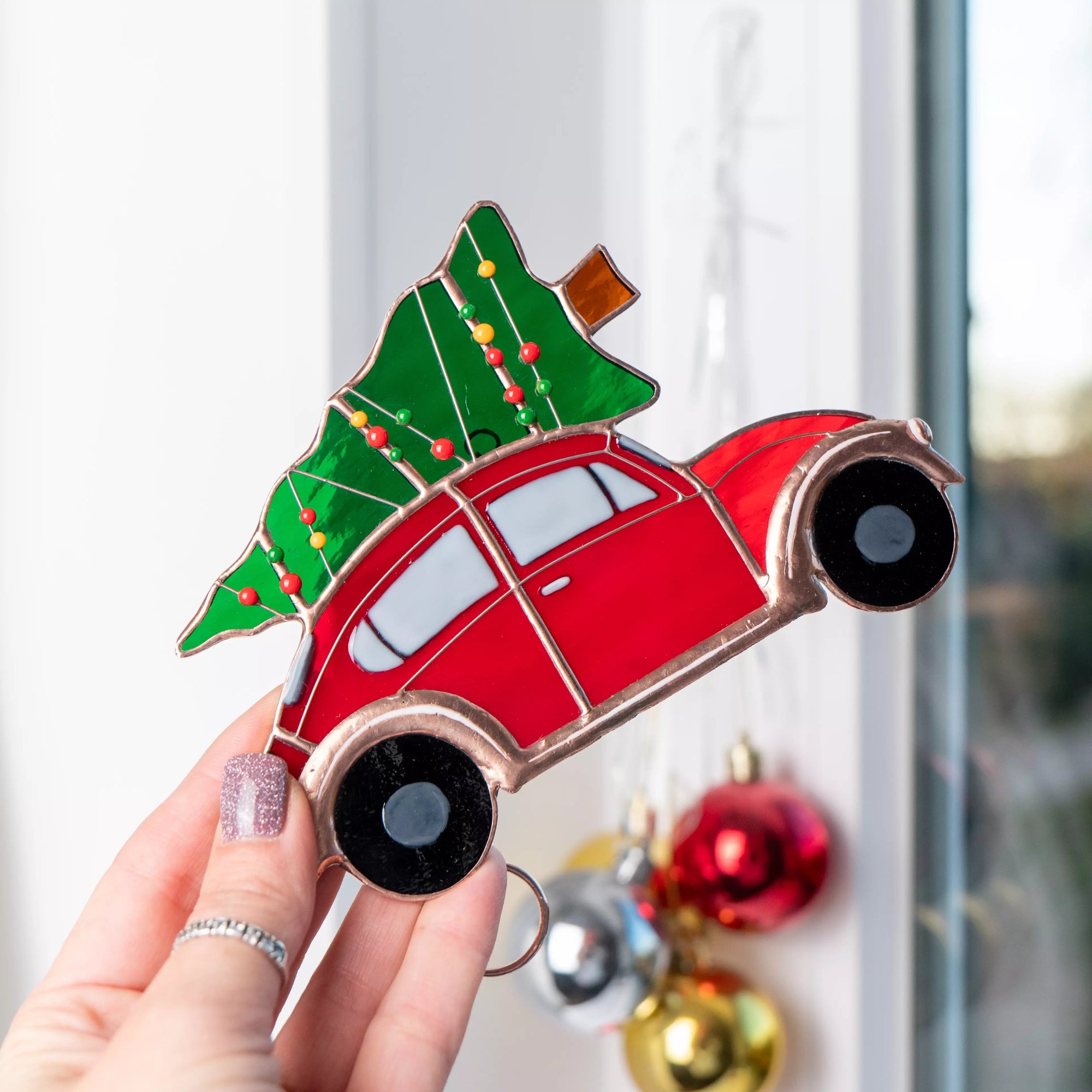 Stained glass window hanging red car with a Christmas tree on top, held by a hand.