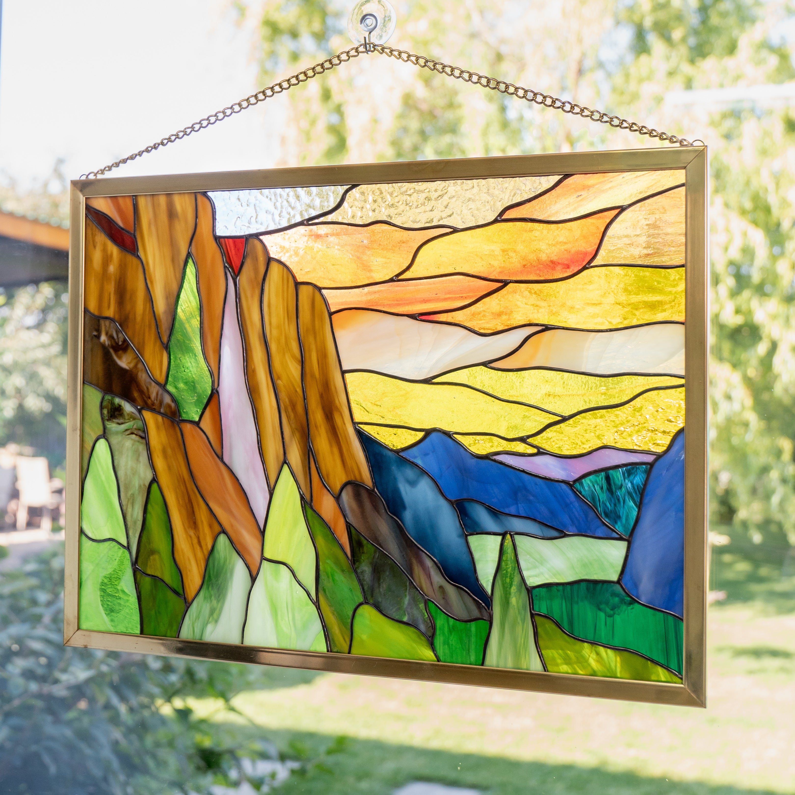 Colorful stained glass Yosemite panel showing granite cliffs, layered hills, and a sunset-inspired sky.