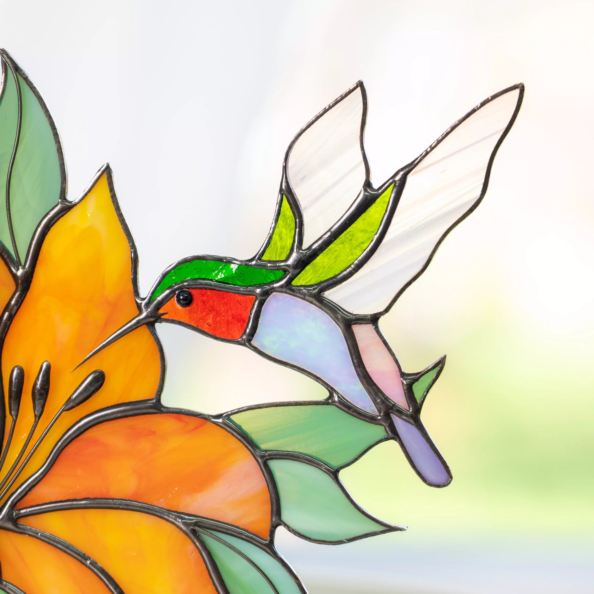 Stained glass panel featuring hummingbird with red throat flying toward an orange flower, detailed glass wings and leaves