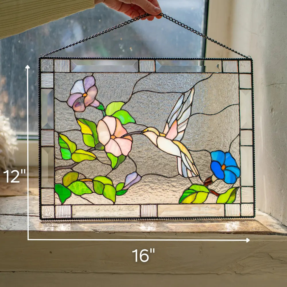Stained glass panel with a hummingbird and flowers, held up against a neutral background with dimensions: 12 x 16 inches