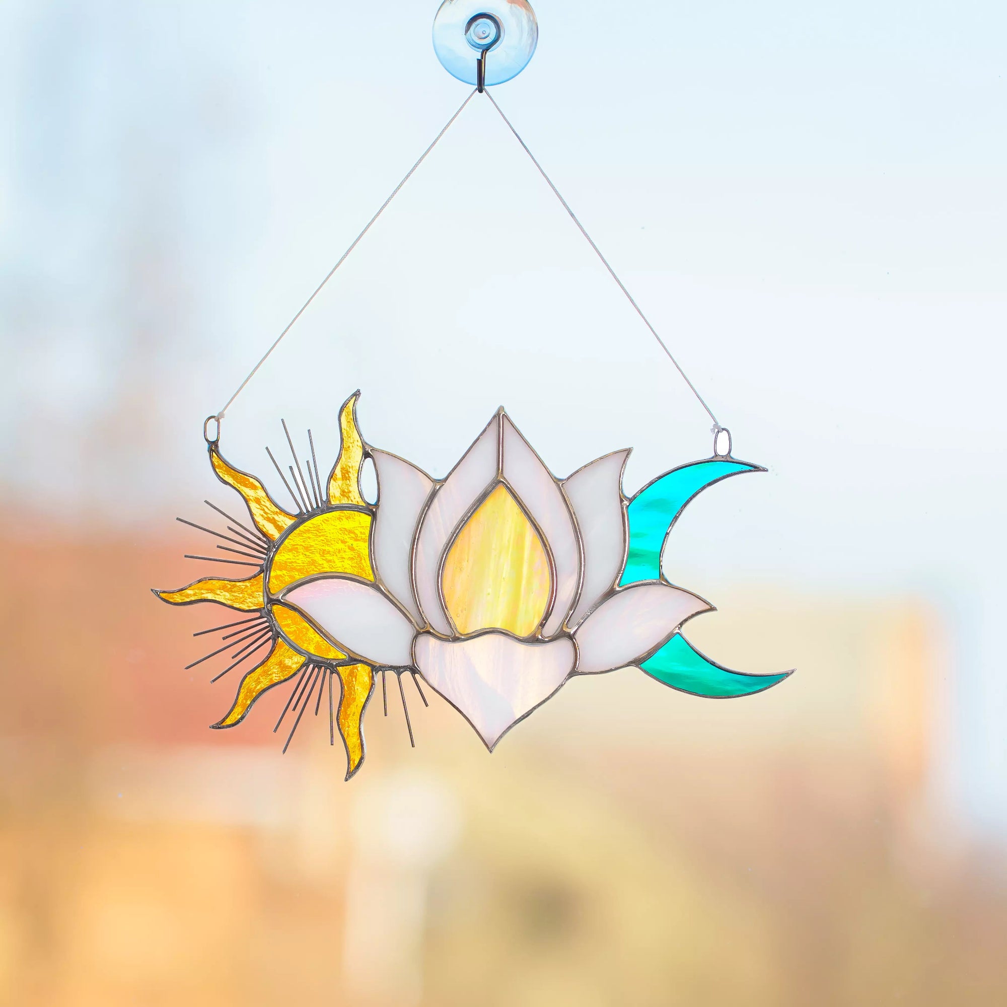 Decorative stained glass suncatcher with sun, moon, and lotus flower design on a blurred background.