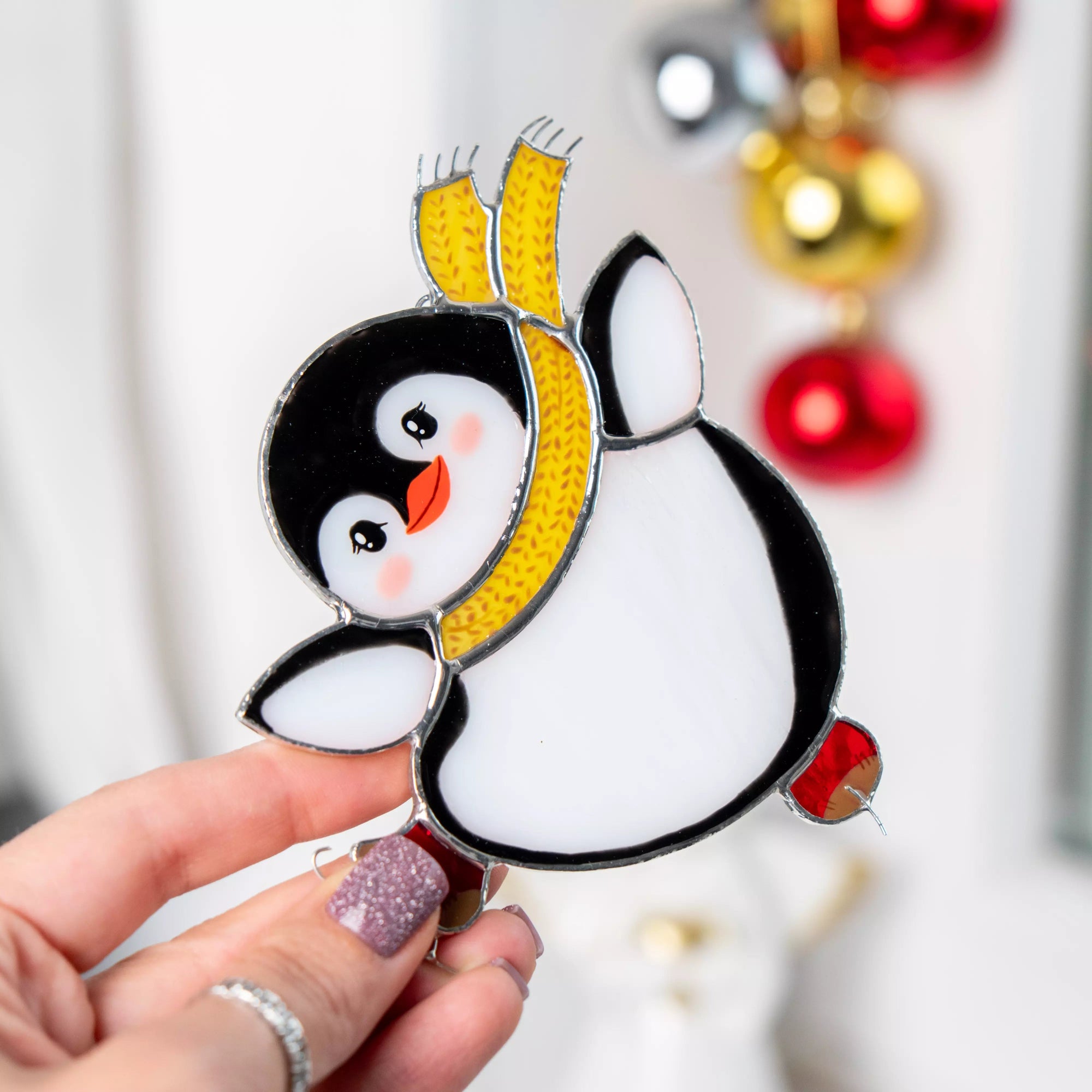 Stained glass penguin Christmas ornament held by a hand with festive decorations in the background