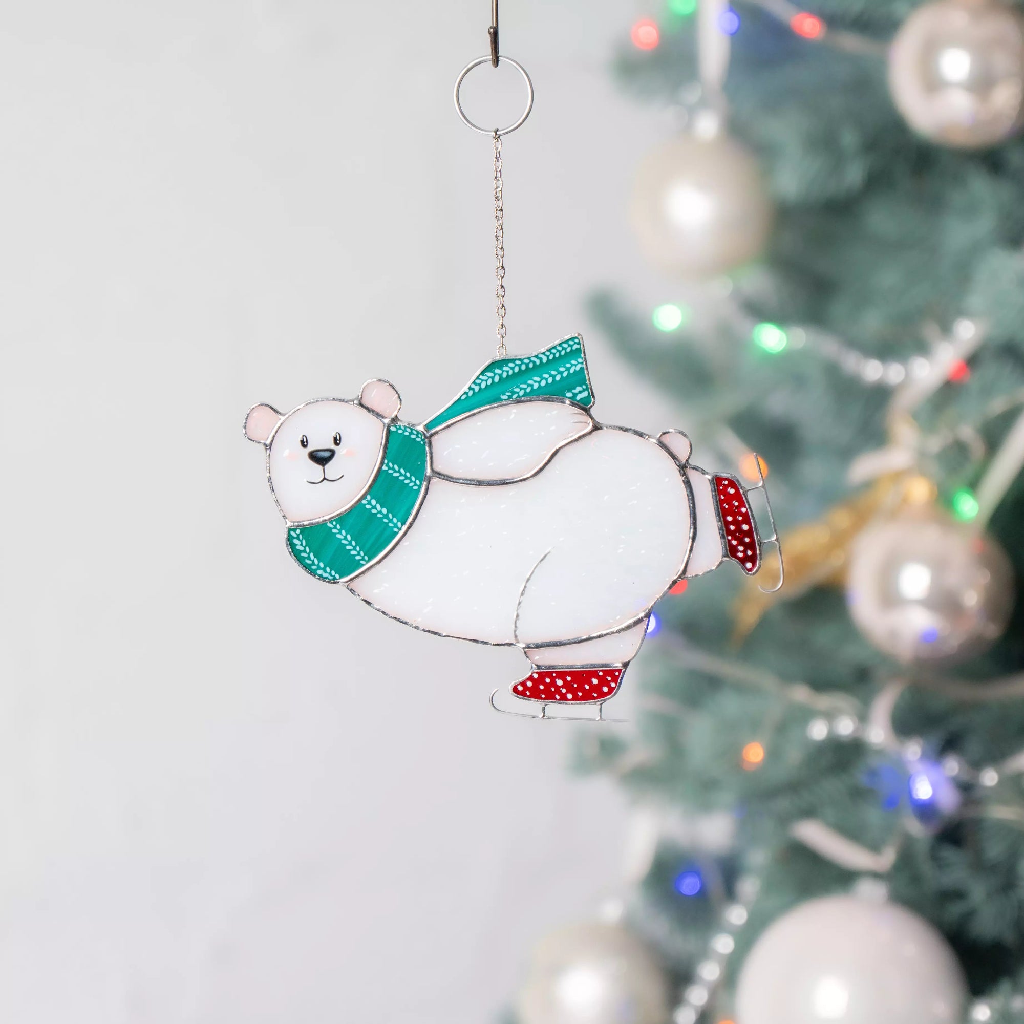 Stained glass suncatcher polar bear on a skates hanging on a Christmas tree with colorful lights and ornaments.