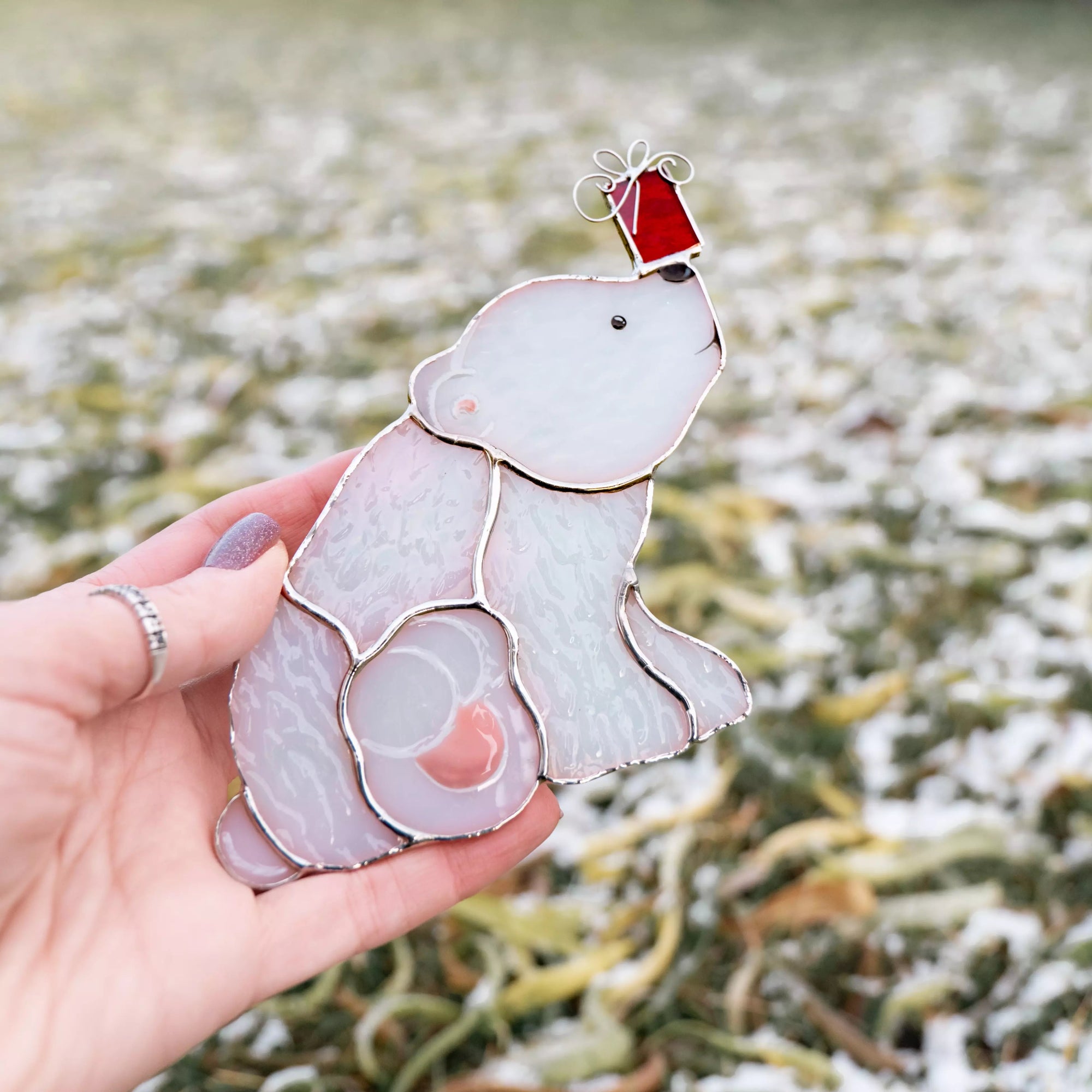 Hand holding a stained glass suncatcher, featuring polar bear with a Christmas gift ornament with a snowy background