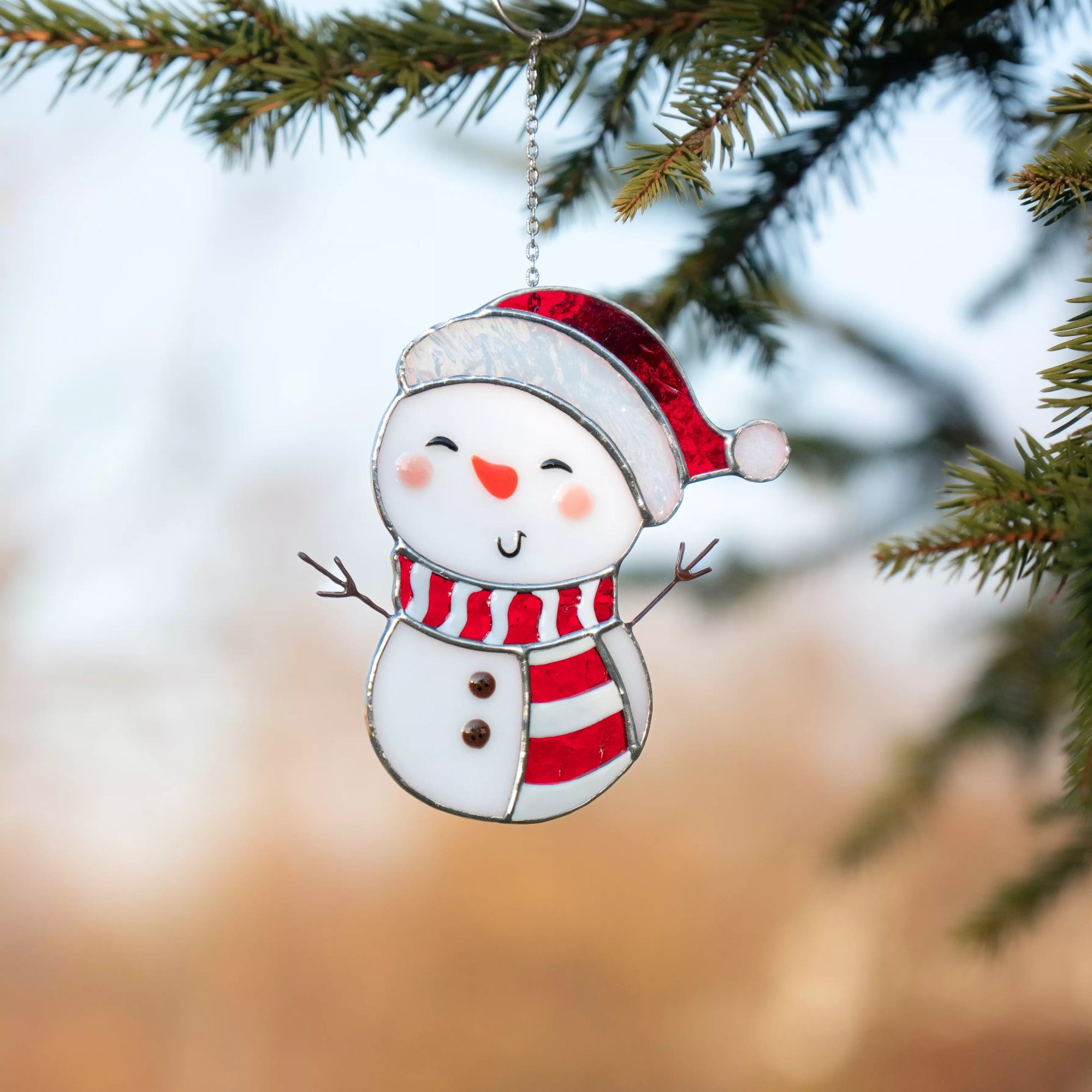 Stained glass window hanging snowman hanging on a tree branch with a blurred natural background
