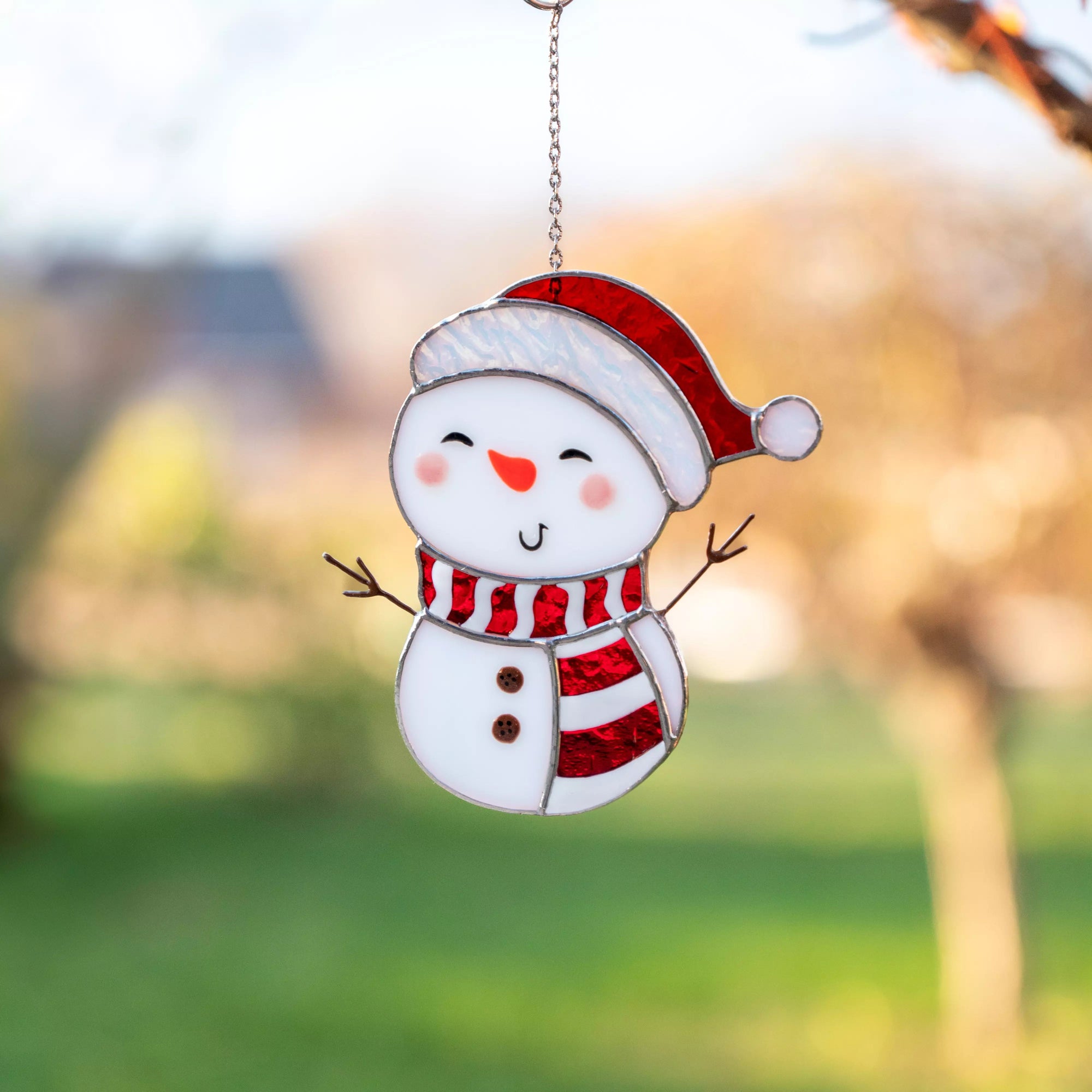Stained glass suncatcher snowman with a red hat and scarf against a blurred outdoor background