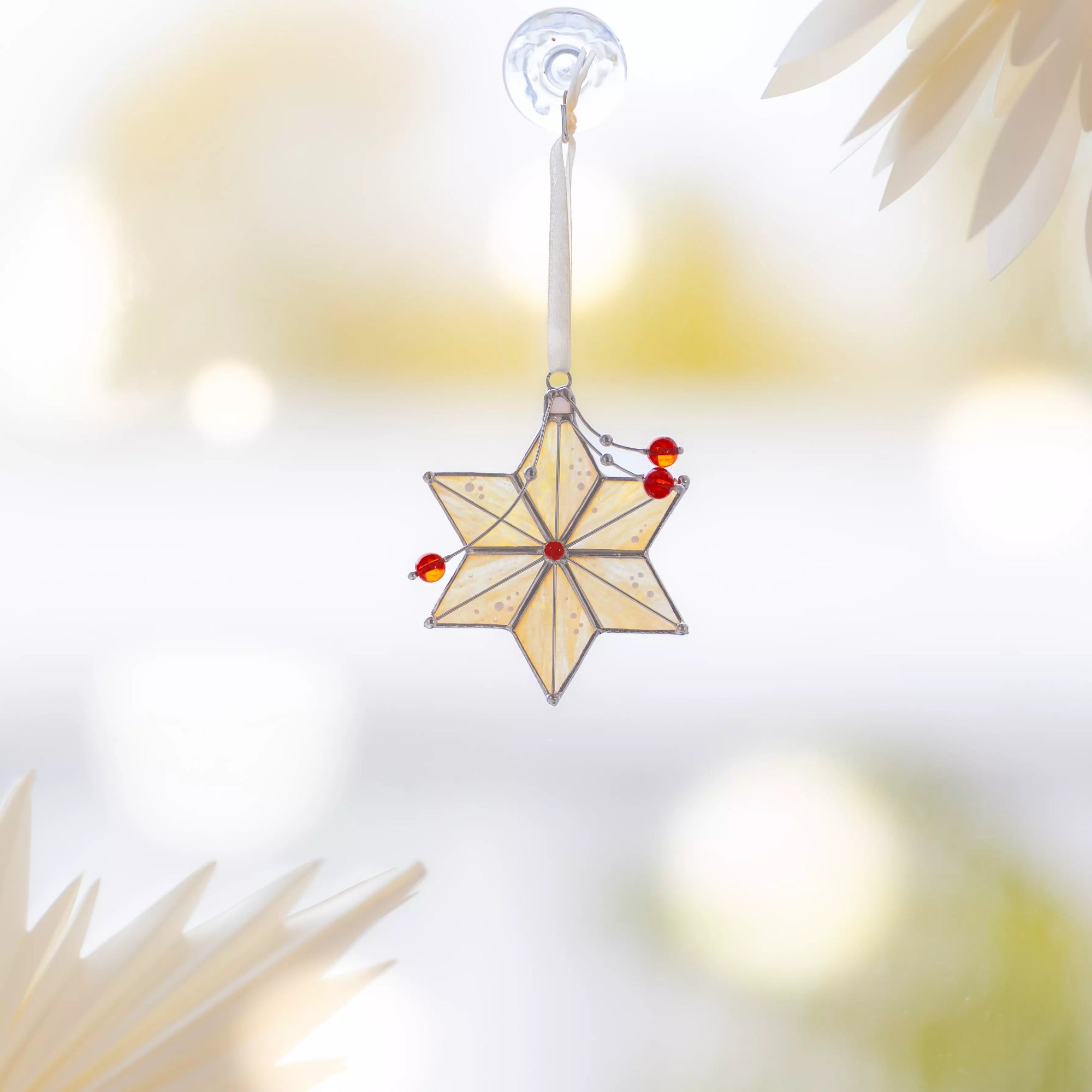 Stained glass star ornament hanging from a window with red beads, sparkling in the light
