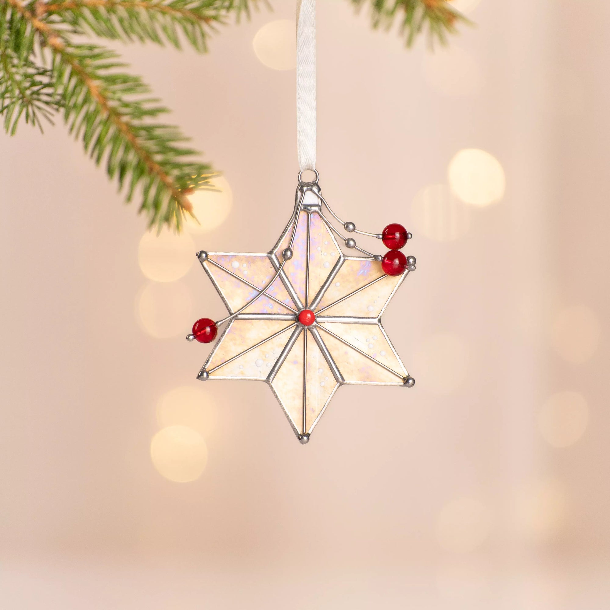 Stained glass star ornament with red beads hanging near a window during the holiday season
