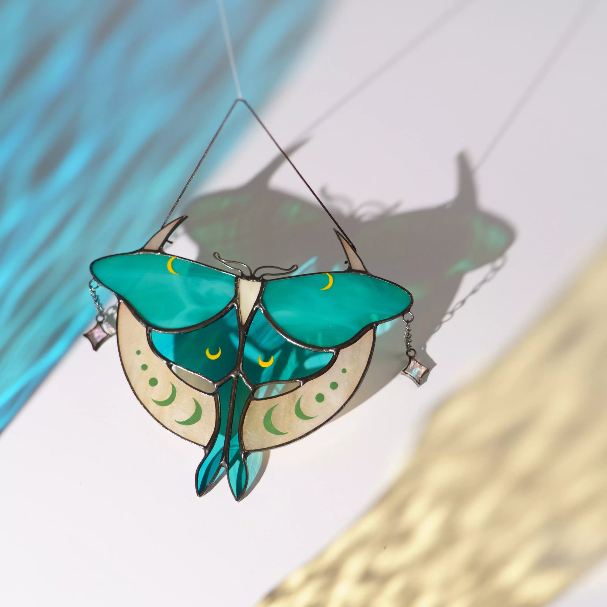 Stained glass luna moth suncatcher casting a colorful shadow on a surface