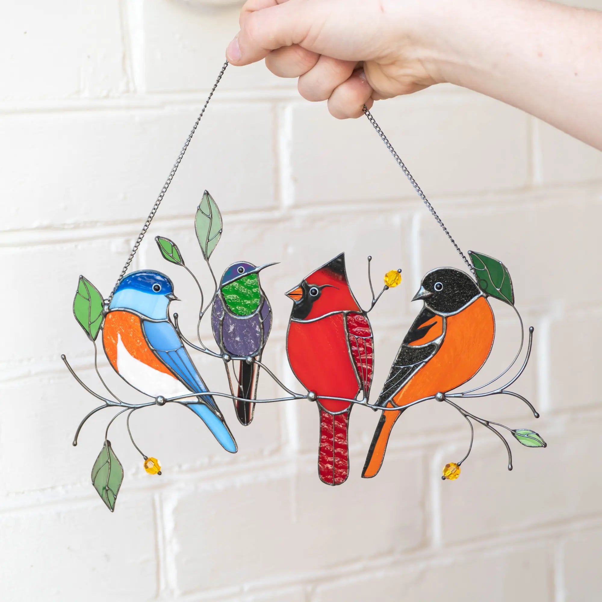Four colorful birds stained glass suncatcher on a white tiled wall background