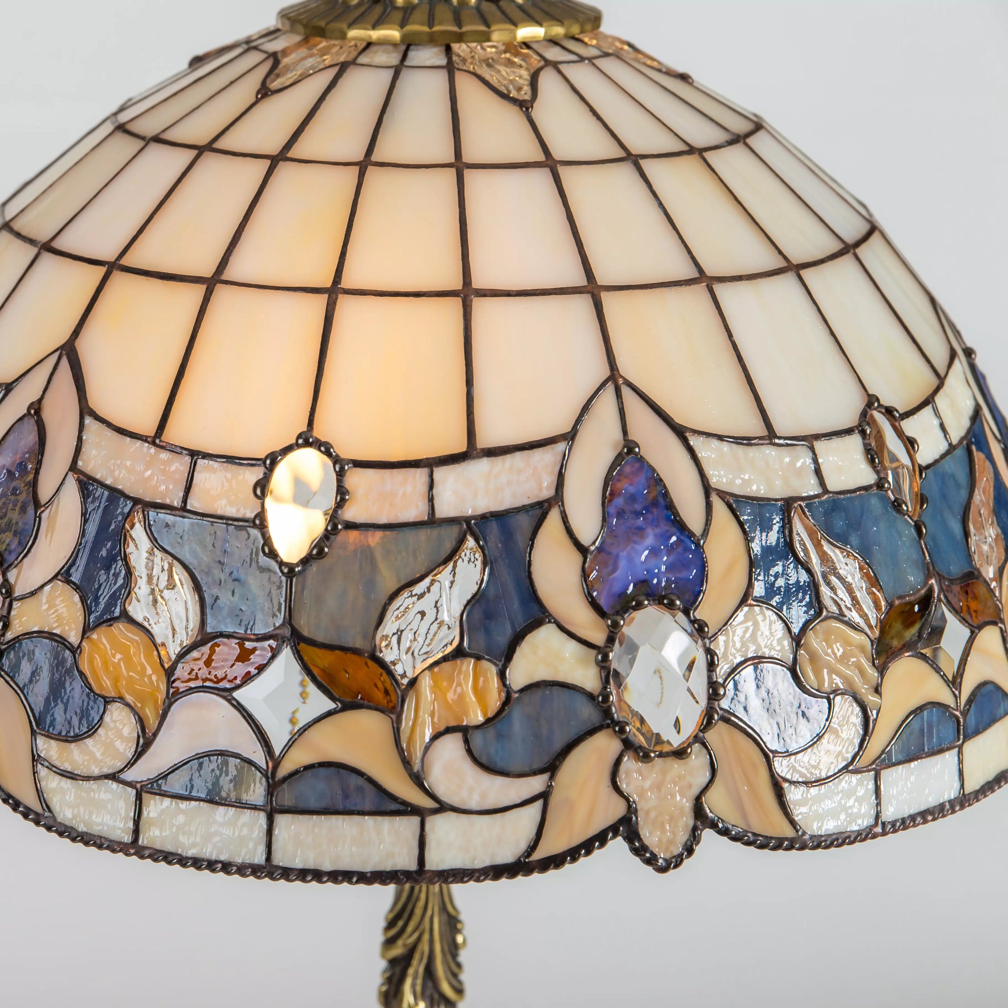 Close-up of stained glass table lamp shade with floral design in blue, amber, and clear glass pieces