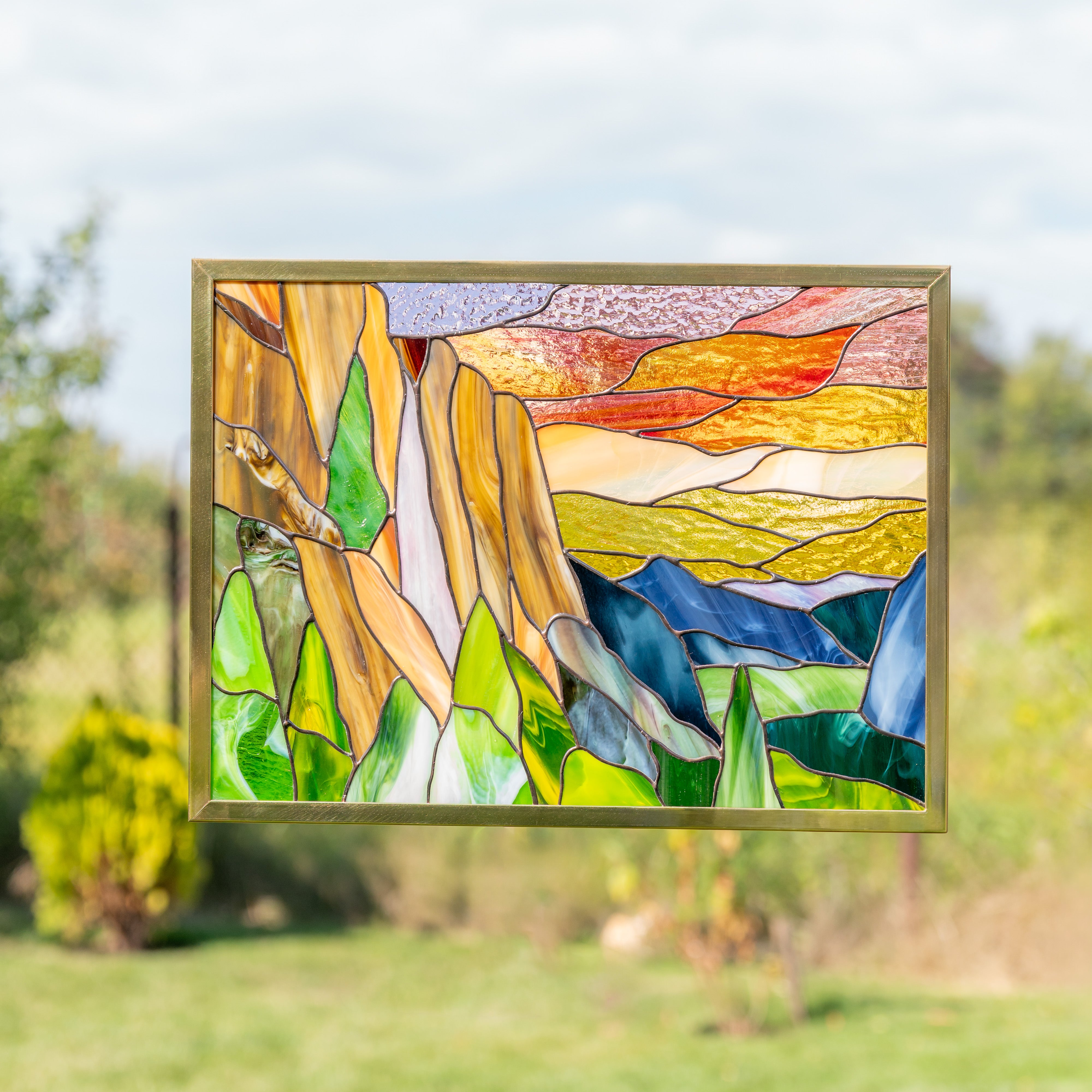 Stained glass Yosemite panel glowing with sunlight, showing vivid landscape details in layered colors.