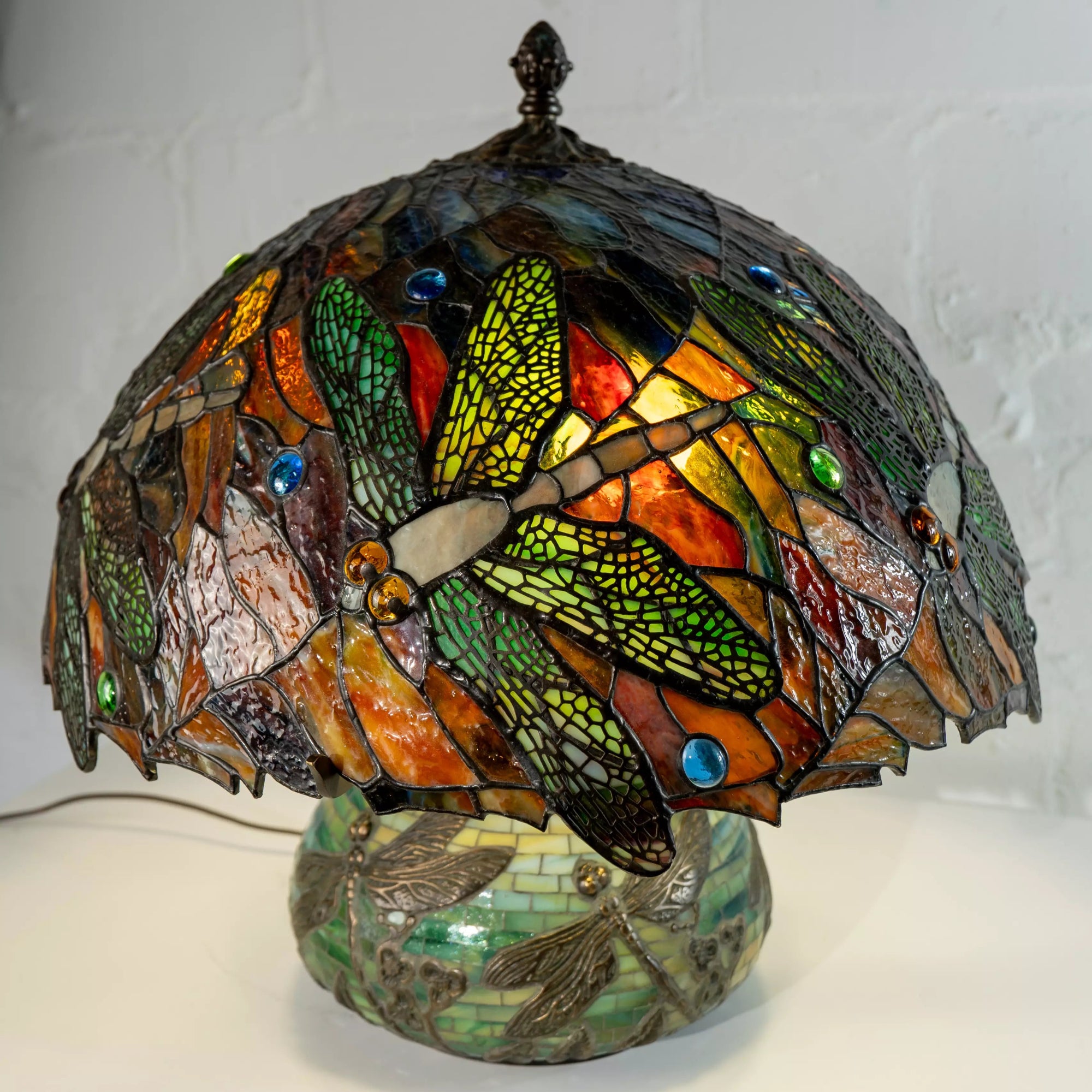 Side view of dragonfly glass lamp with bronze top and glowing dome in multicolor stained glass
