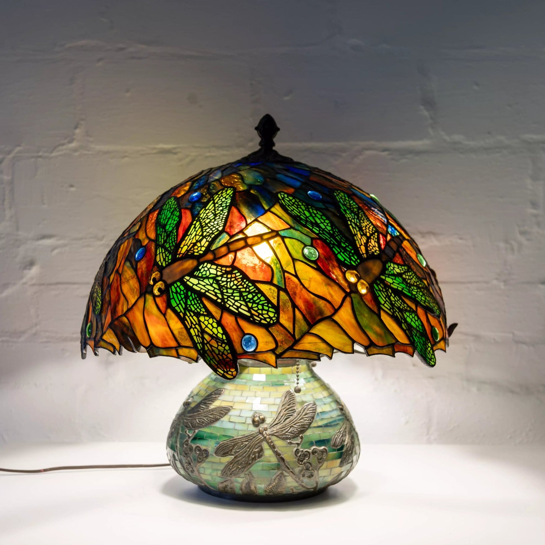 Dragonfly lamp turned on, glowing in yellow, orange and green with dark green base