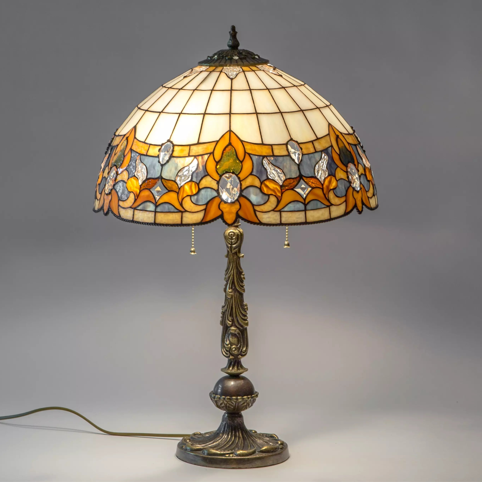 Full view of stained glass table lamp with amber, beige, and clear dome and ornate bronze-tone stand